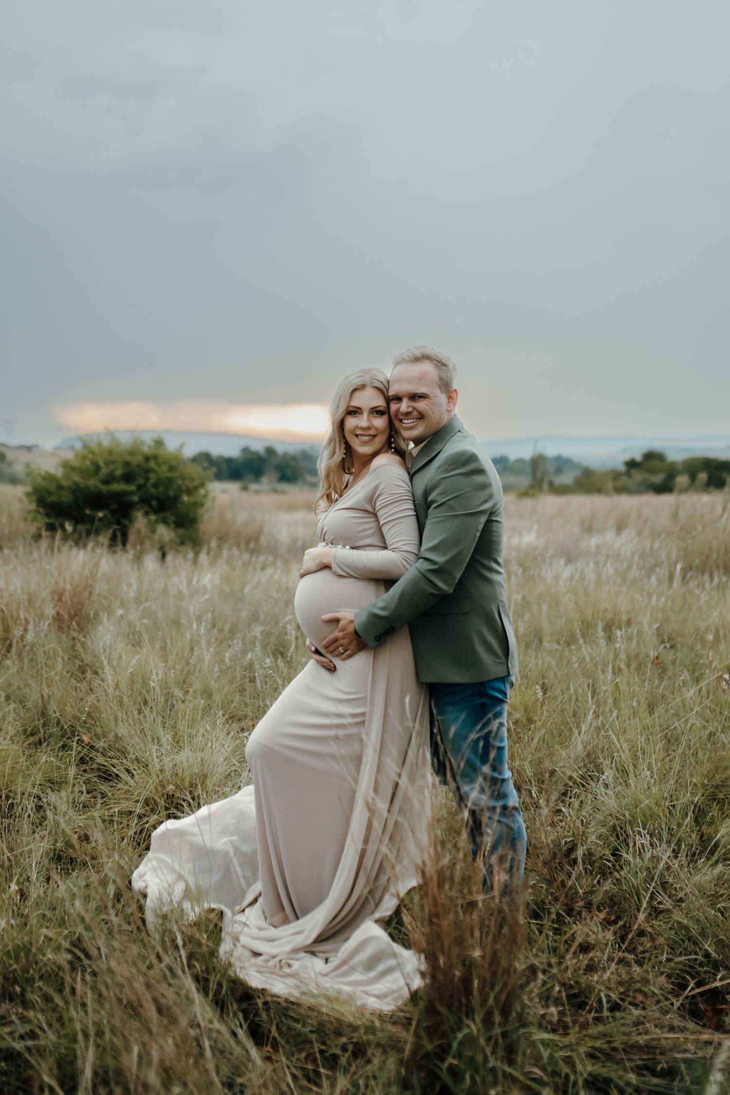 A couple embraces lovingly in a rustic field with tall grass during a romantic outdoor photo session.
