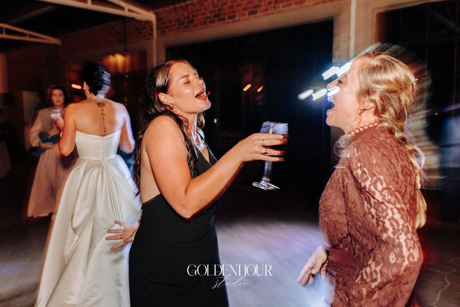 Two women laughing and celebrating with wine glasses on the wedding reception dance floor.