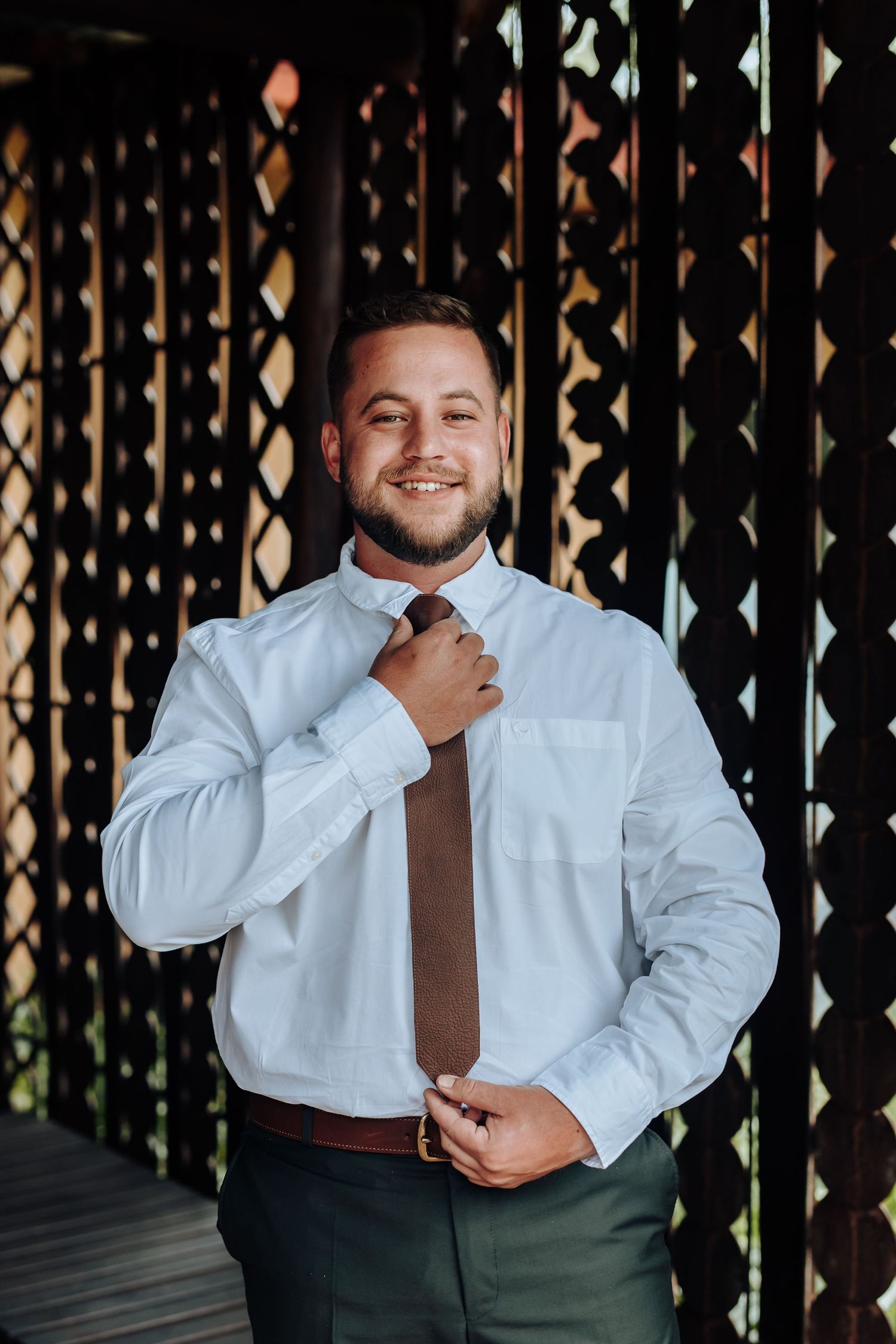 Four sequential photos show someone adjusting a brown tie against a white dress shirt with a decorative lattice background.