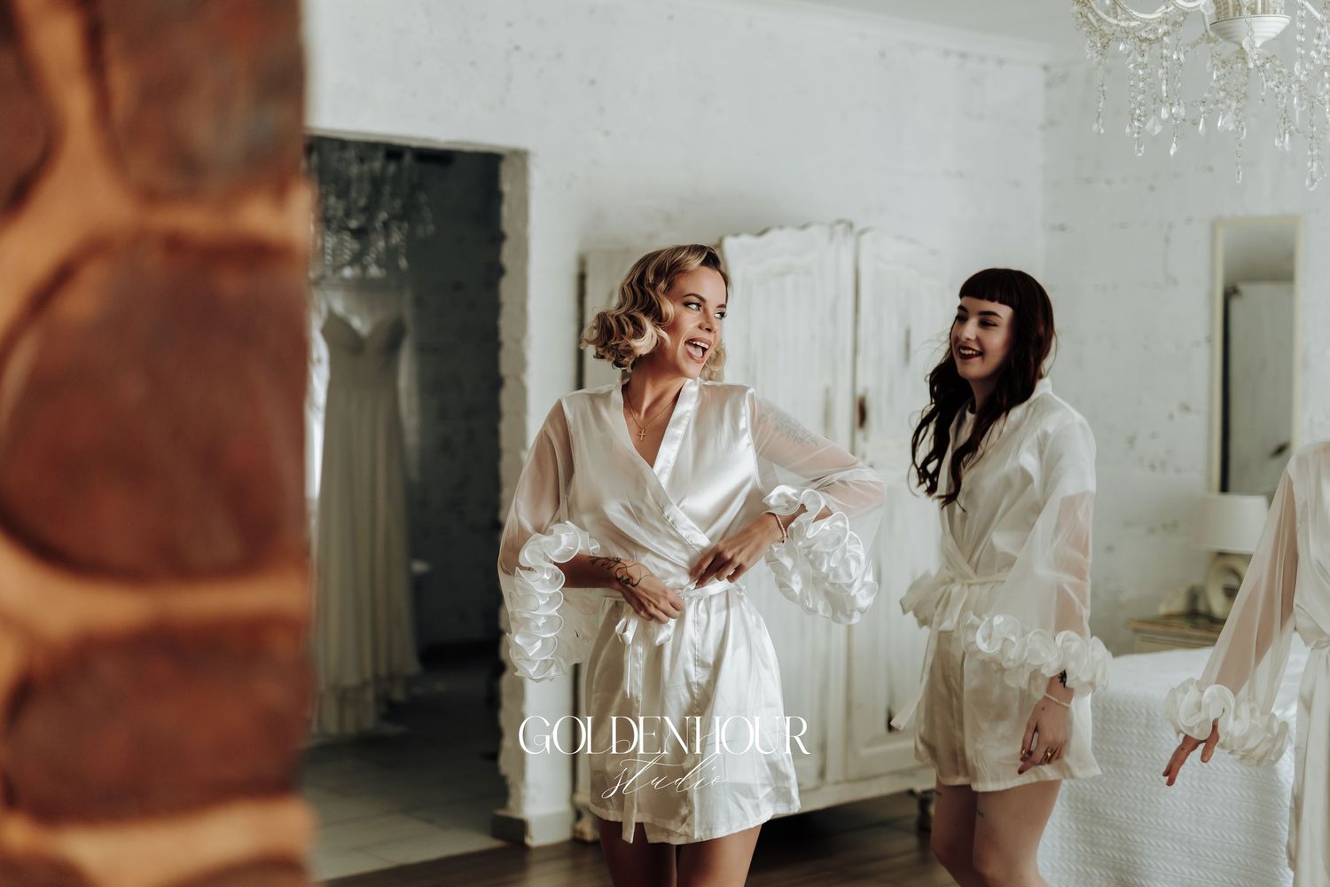 Bridesmaids in white silk robes celebrate with champagne during pre-wedding preparations.
