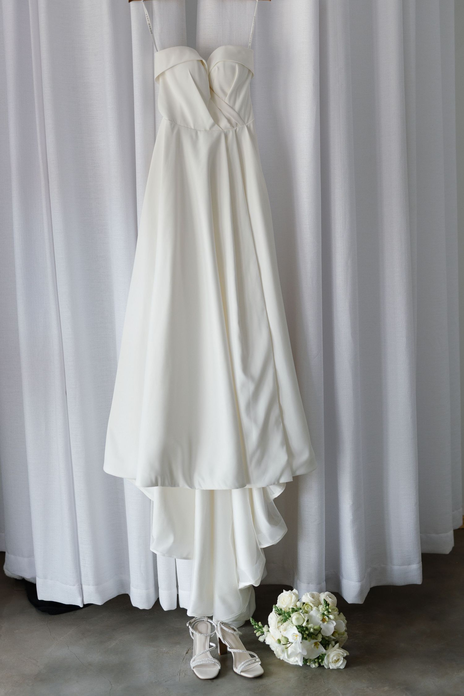Wedding dress detail shots showing white gown hem, bridal shoes and bouquet against light curtain backdrop.