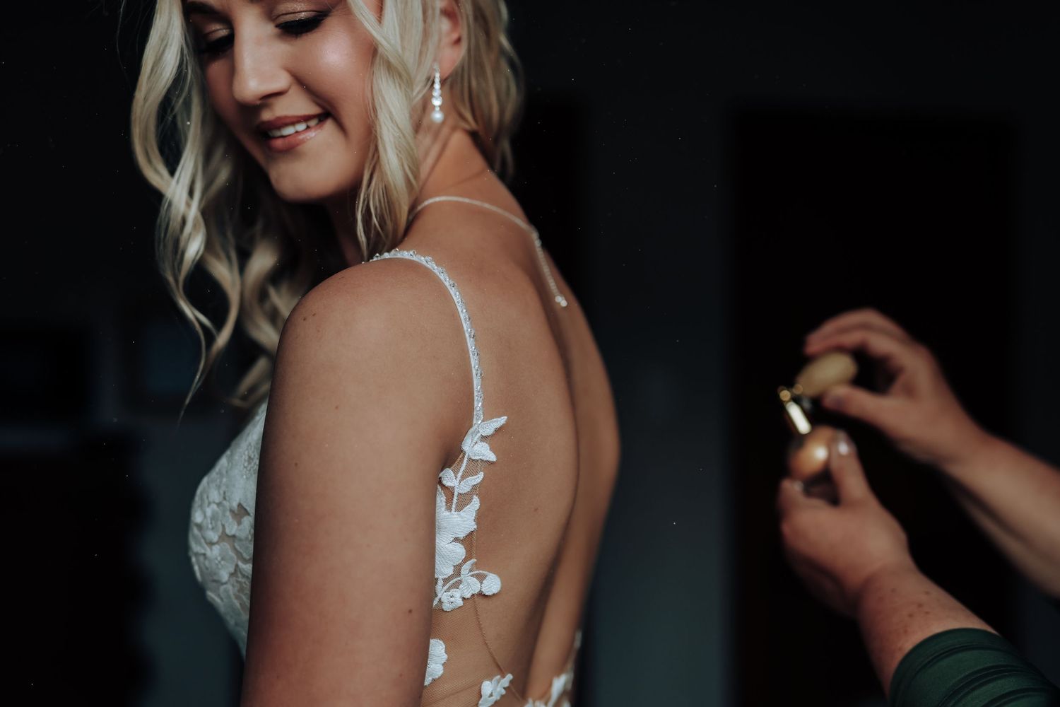 Bride getting ready for wedding day with makeup artist applying finishing touches in dark room.