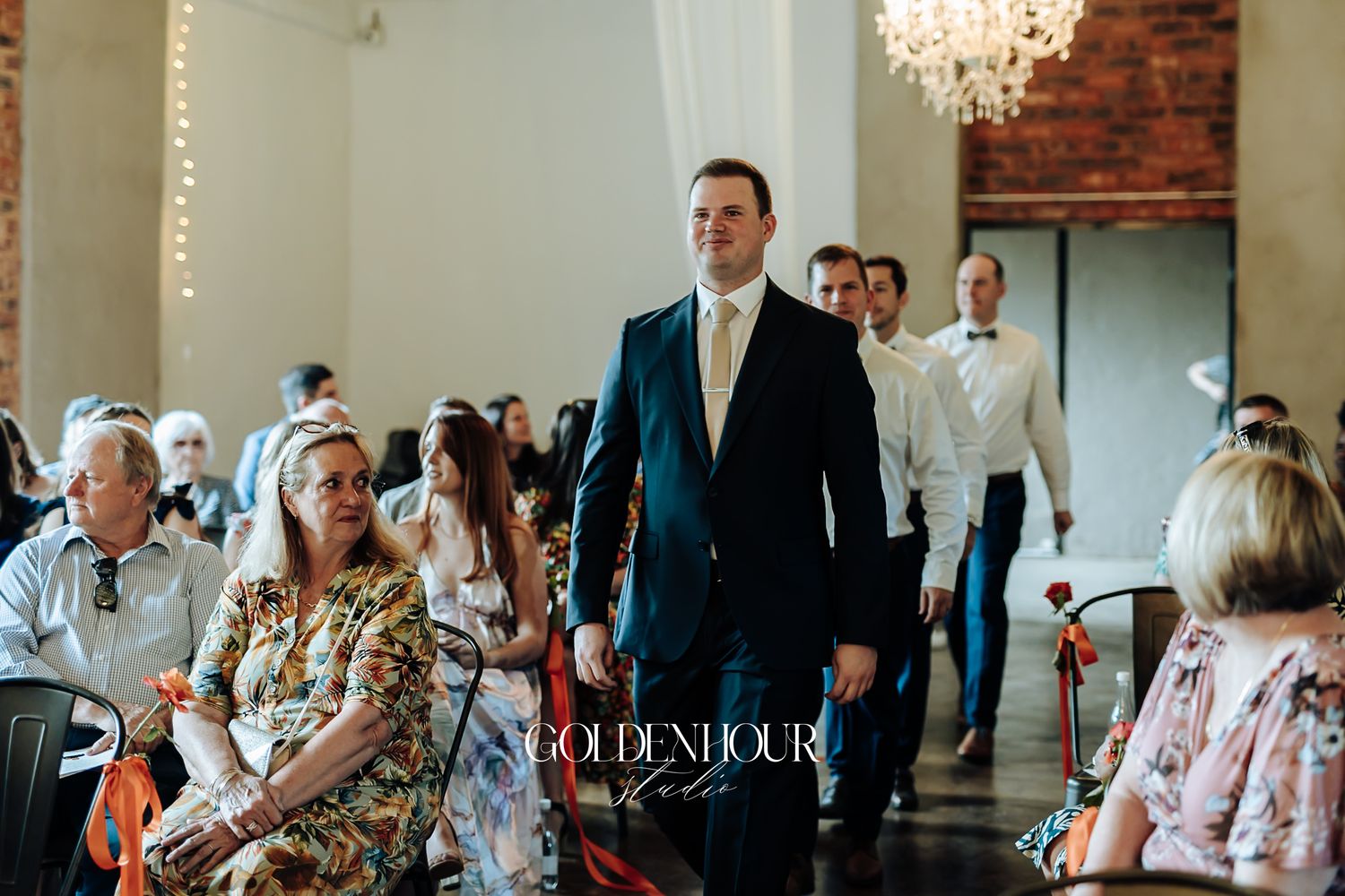 Groom in a navy suit walking down the aisle at an elegant wedding ceremony.