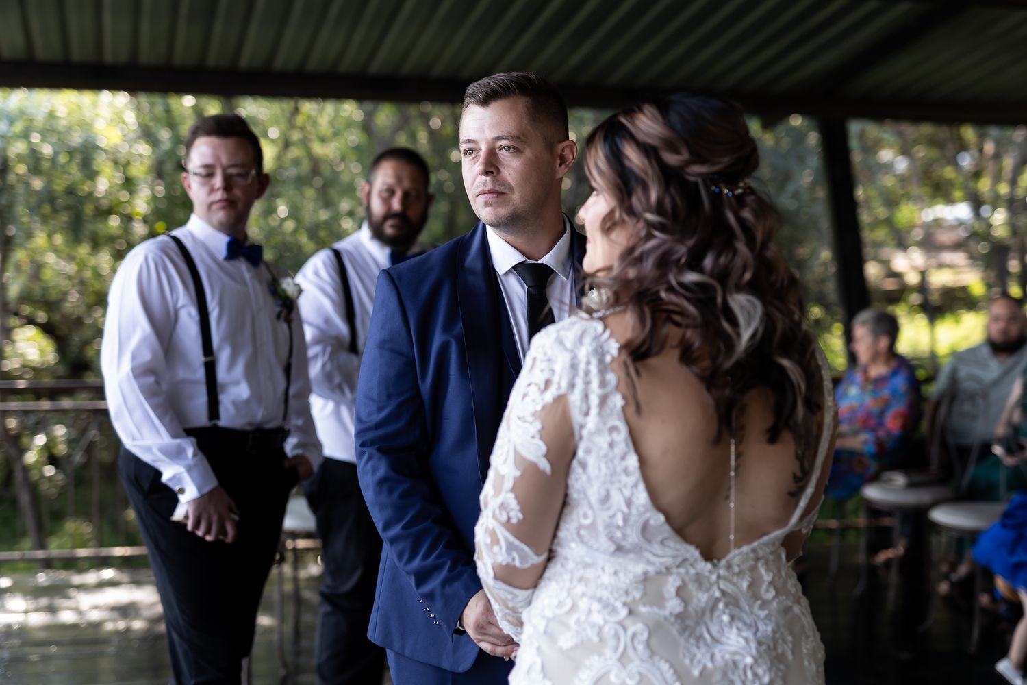 A couple exchanging vows during an outdoor wedding ceremony under a covered pavilion.