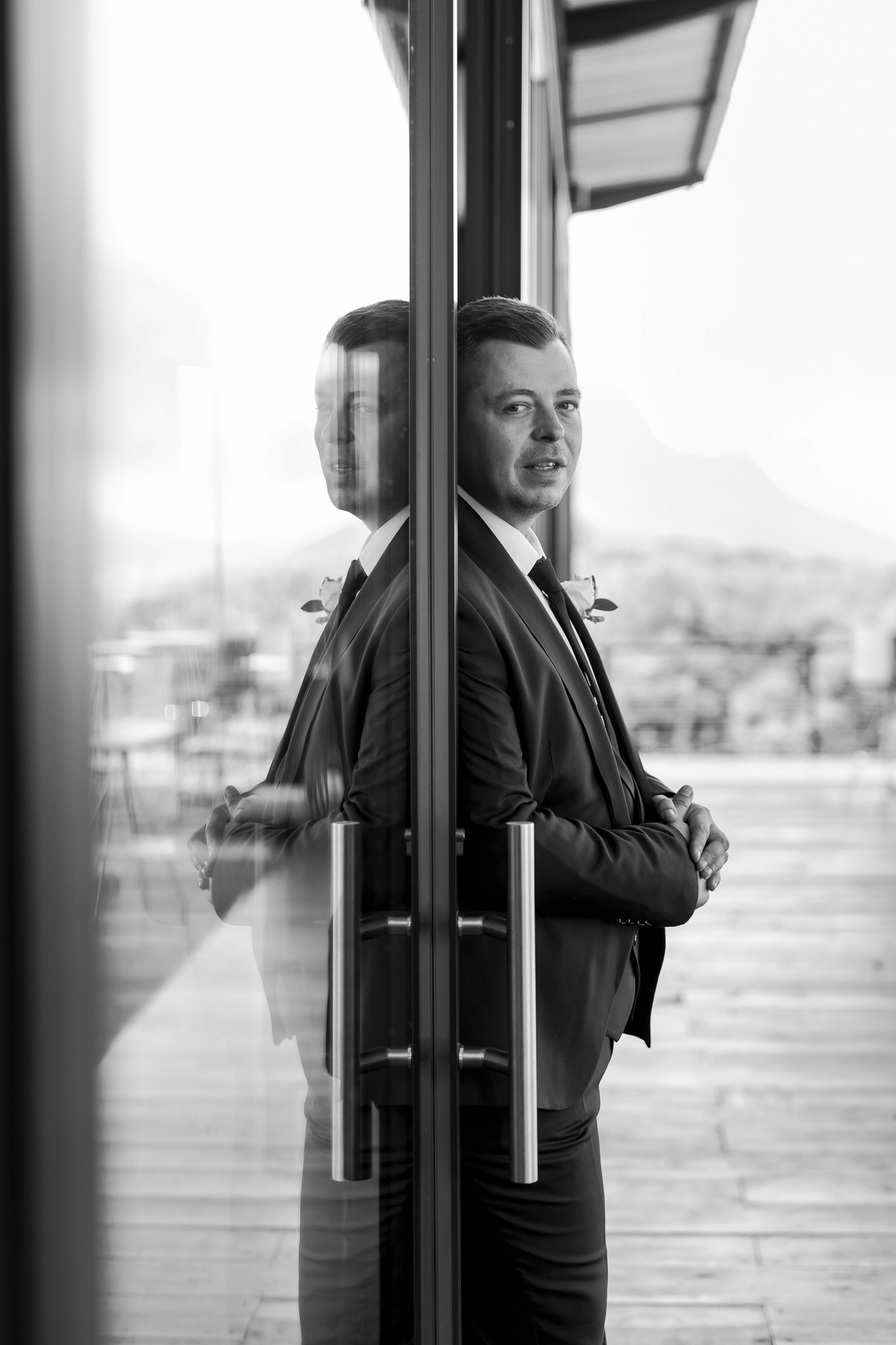 Artistic black and white reflection portrait of groom against glass doors.