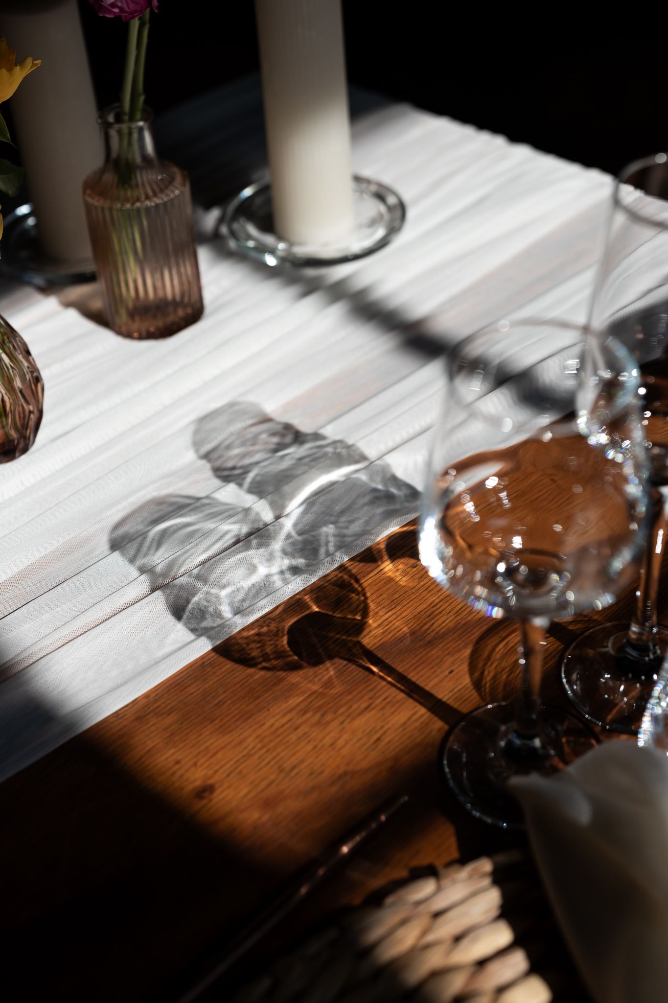 Dramatic shadows cast across a white tablecloth with wine glasses and candlesticks.
