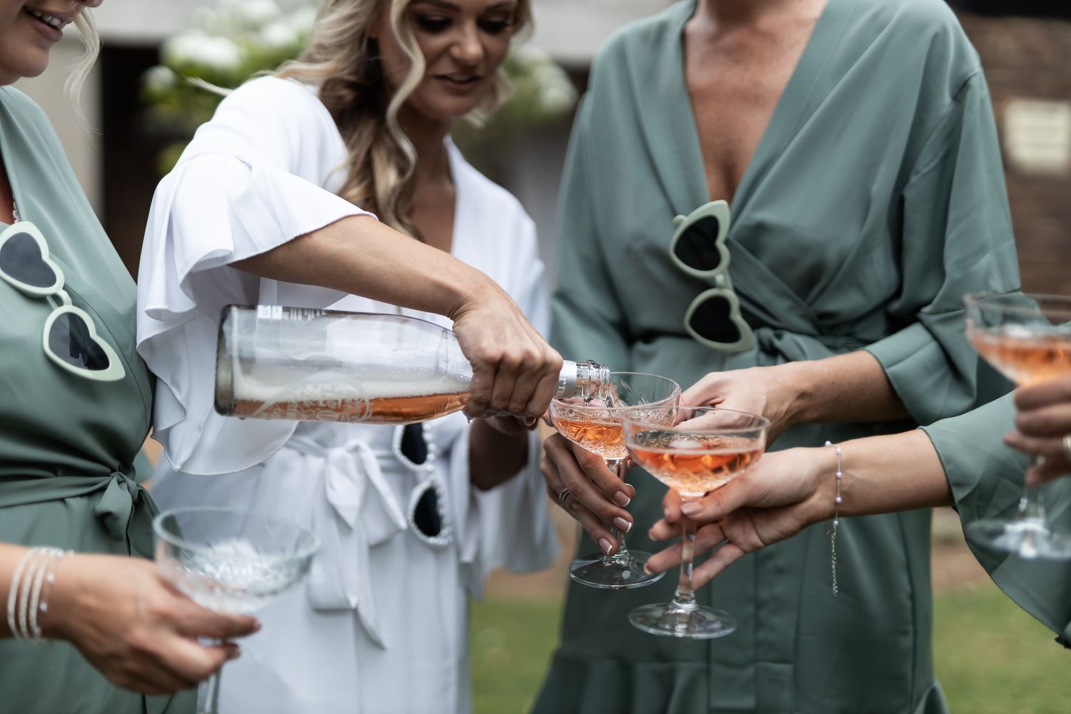 Someone pours champagne into glasses held by people wearing matching sage green robes.