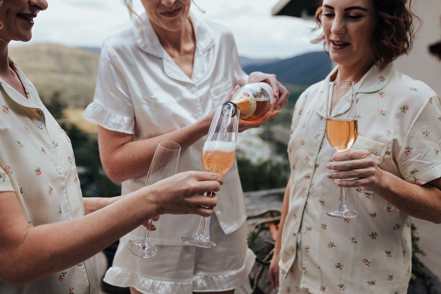 Friends pouring champagne while celebrating outdoors in matching white outfits.