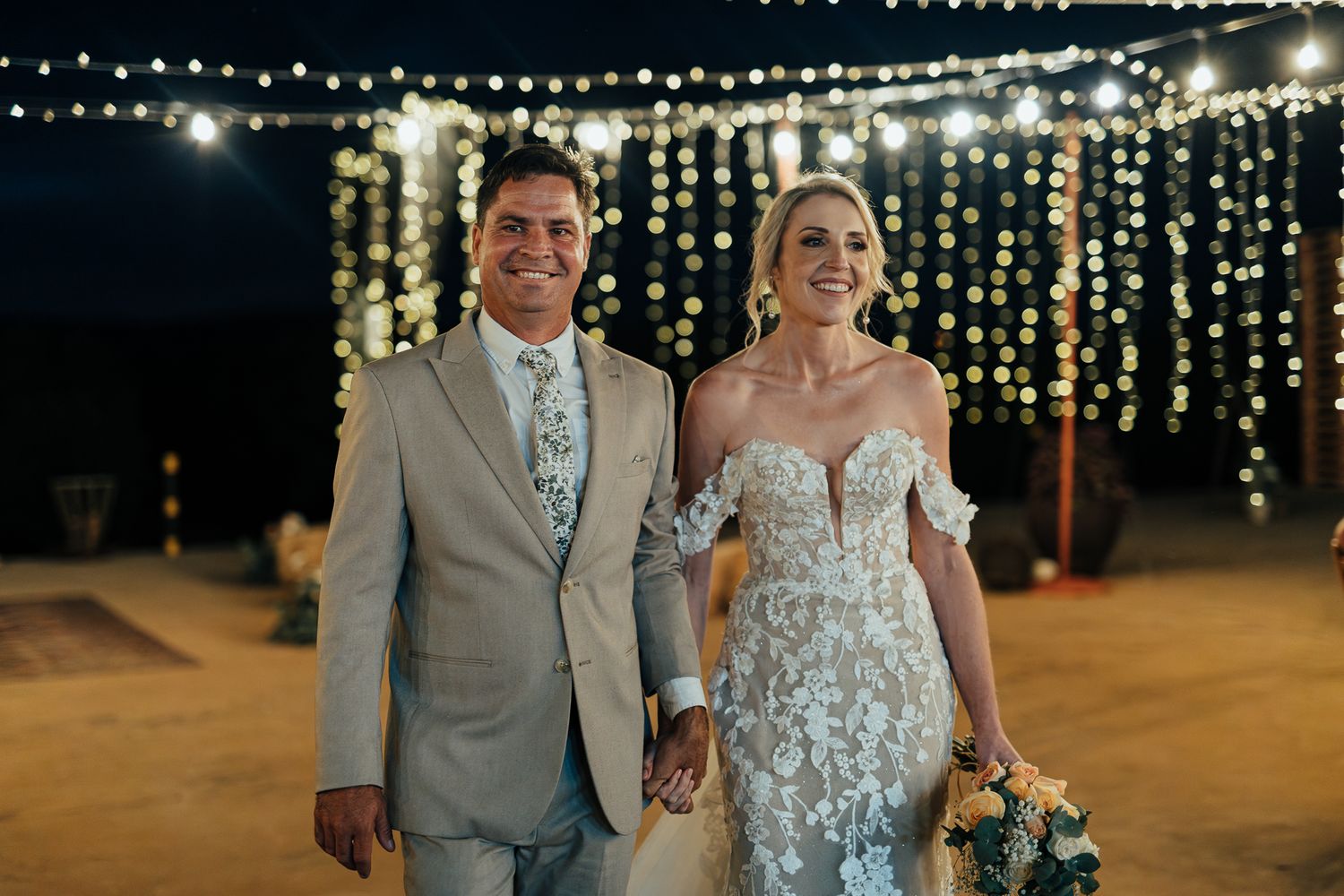 Newlyweds walking together under romantic string light decorations at their reception.