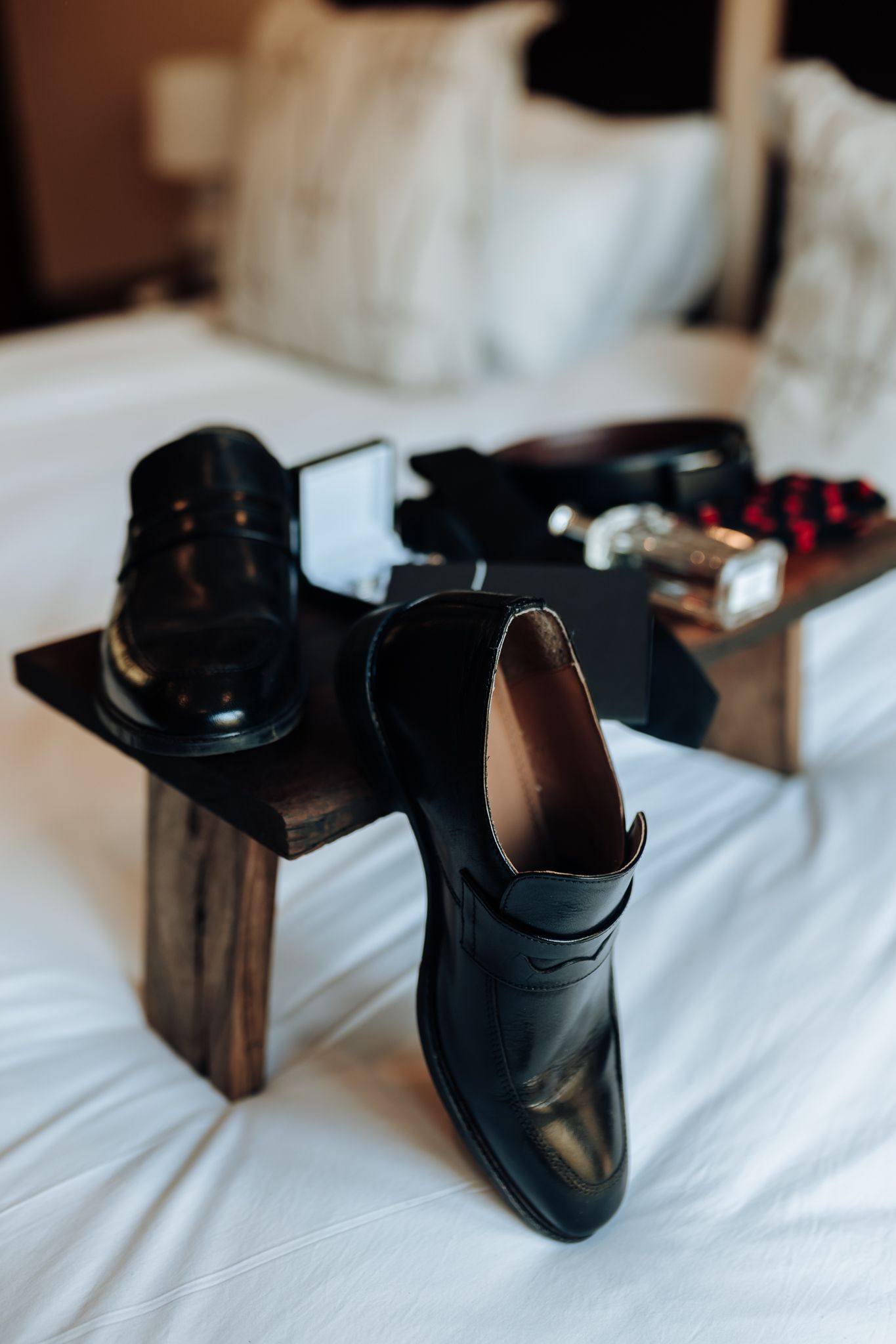 Black leather dress shoes displayed on white bedding with wooden accent.