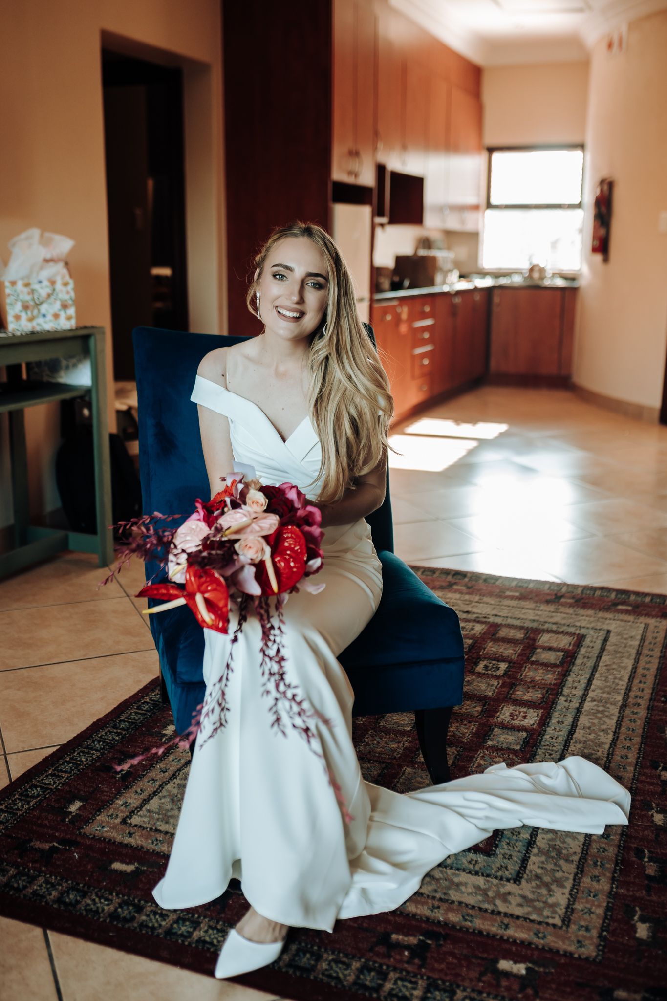 Stunning bridal portrait with vibrant red bouquet while seated in navy blue chair.