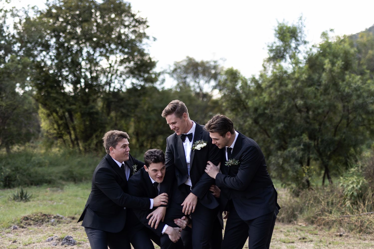 Groomsmen share a candid laughing moment together outdoors during a wedding celebration.