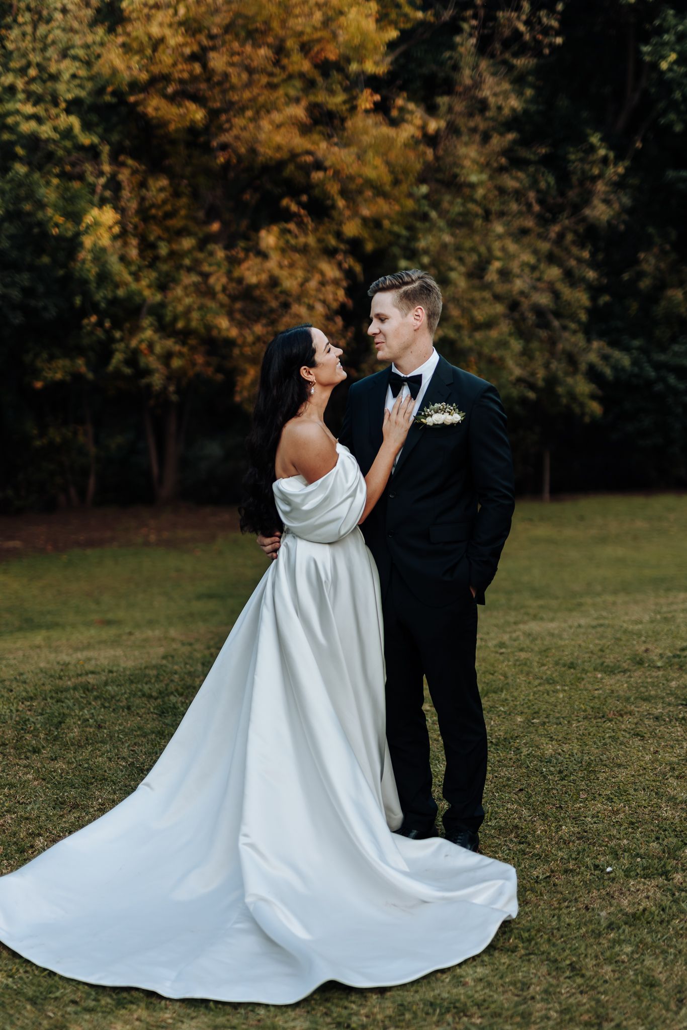 Wedding couple shares intimate moment outdoors with autumn foliage in background.