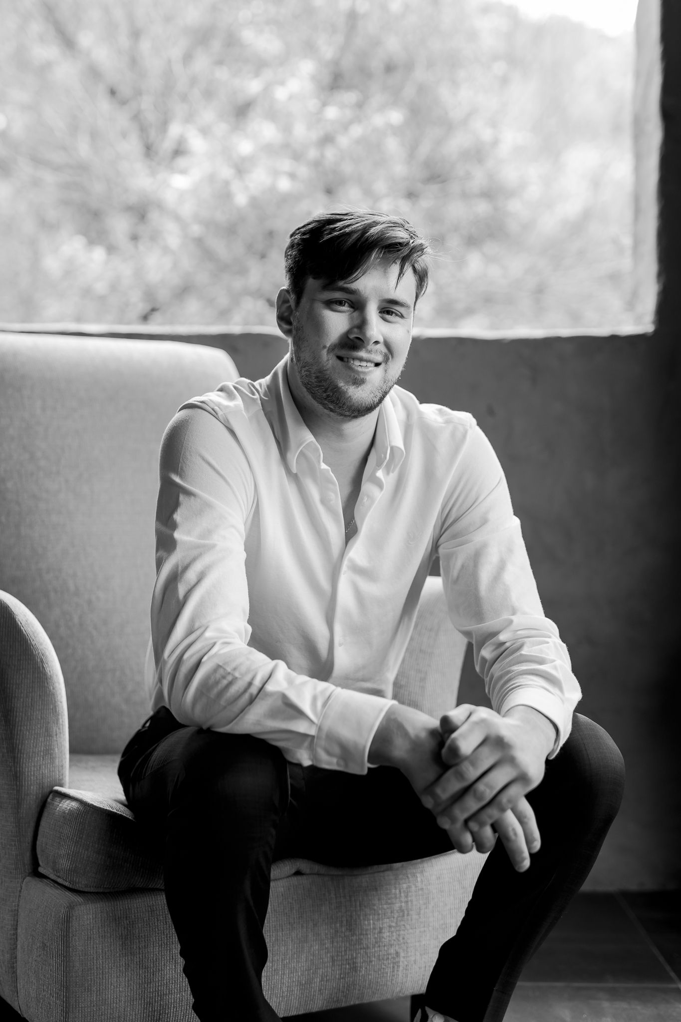 Black and white portrait of man in white shirt sitting casually on armchair.