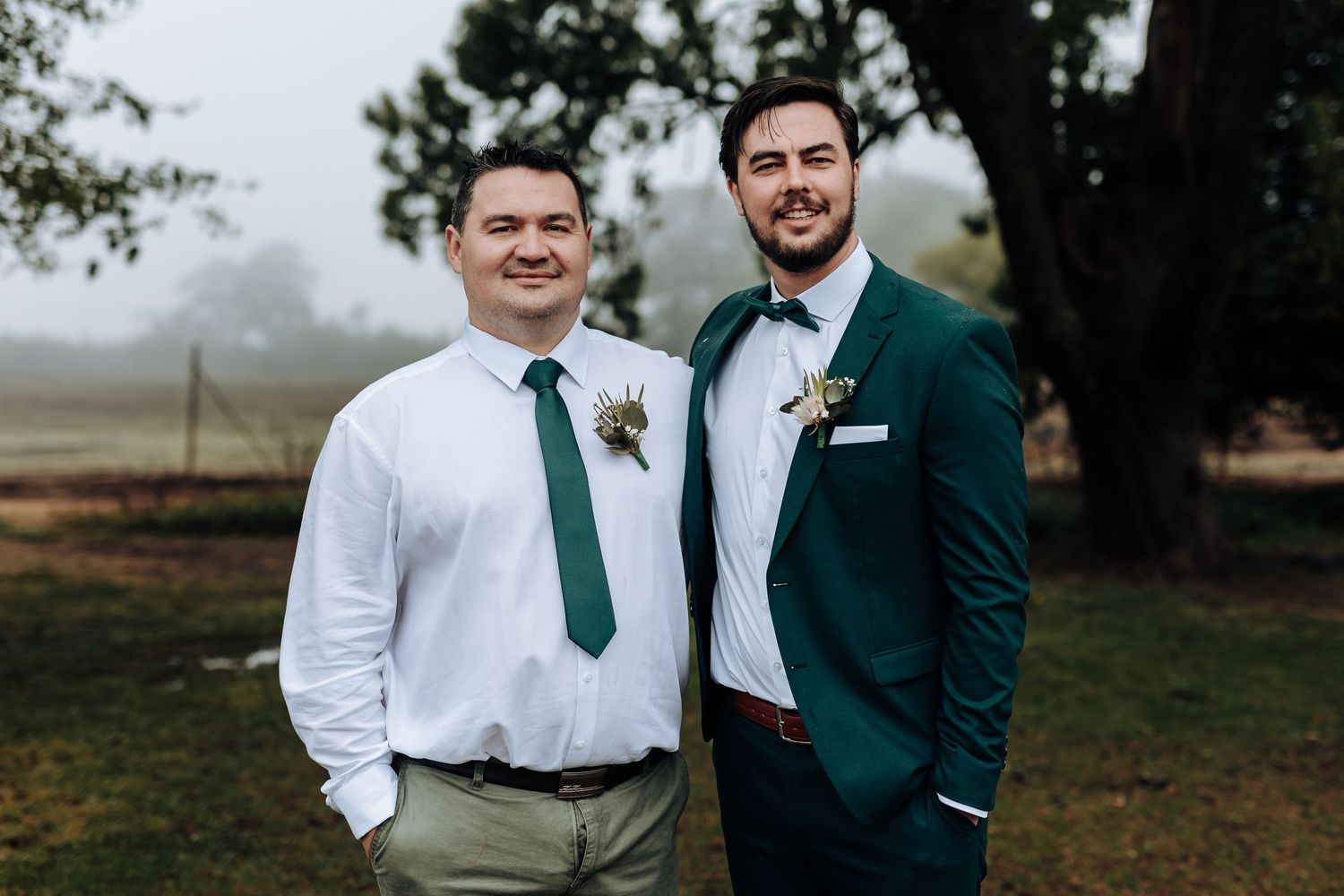 Two members of wedding party stand together against misty outdoor backdrop.