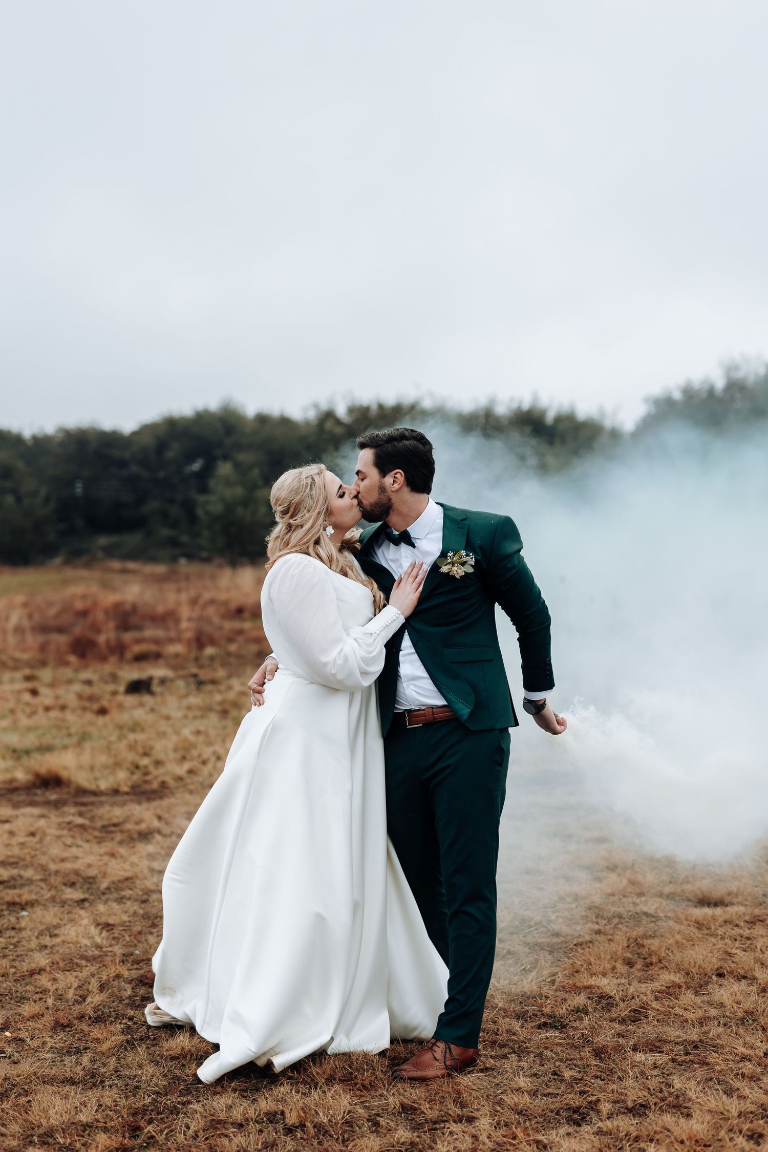 Romantic wedding portrait with atmospheric smoke effects in a rustic field setting.