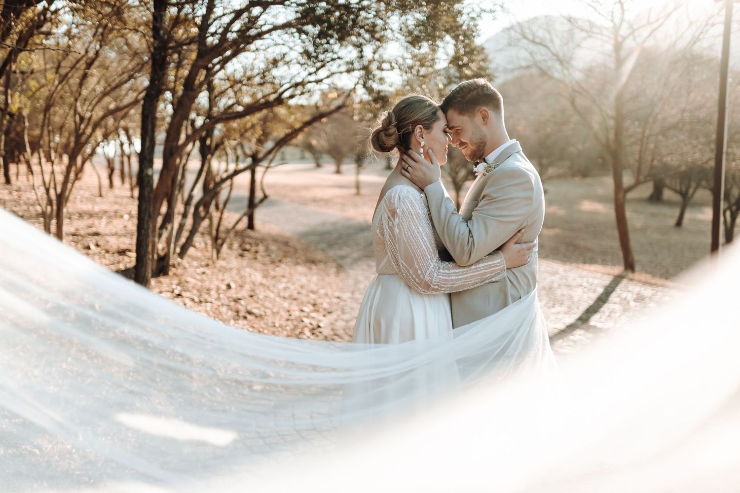 Romantic wedding portrait with flowing veil captured in golden sunlight.