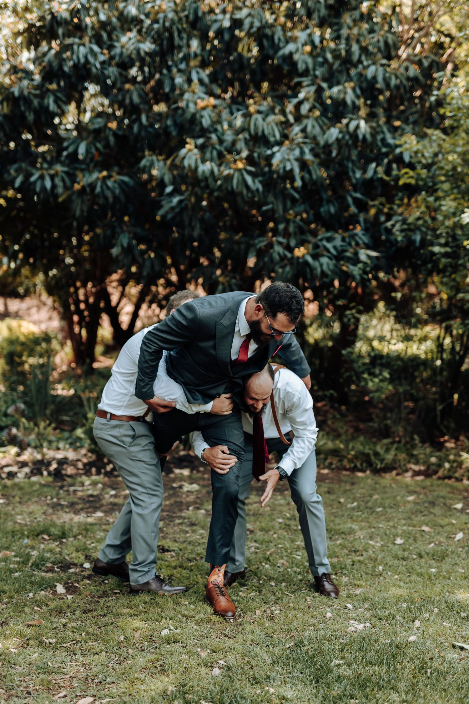 Candid moment of groomsmen horsing around during outdoor wedding photo session.