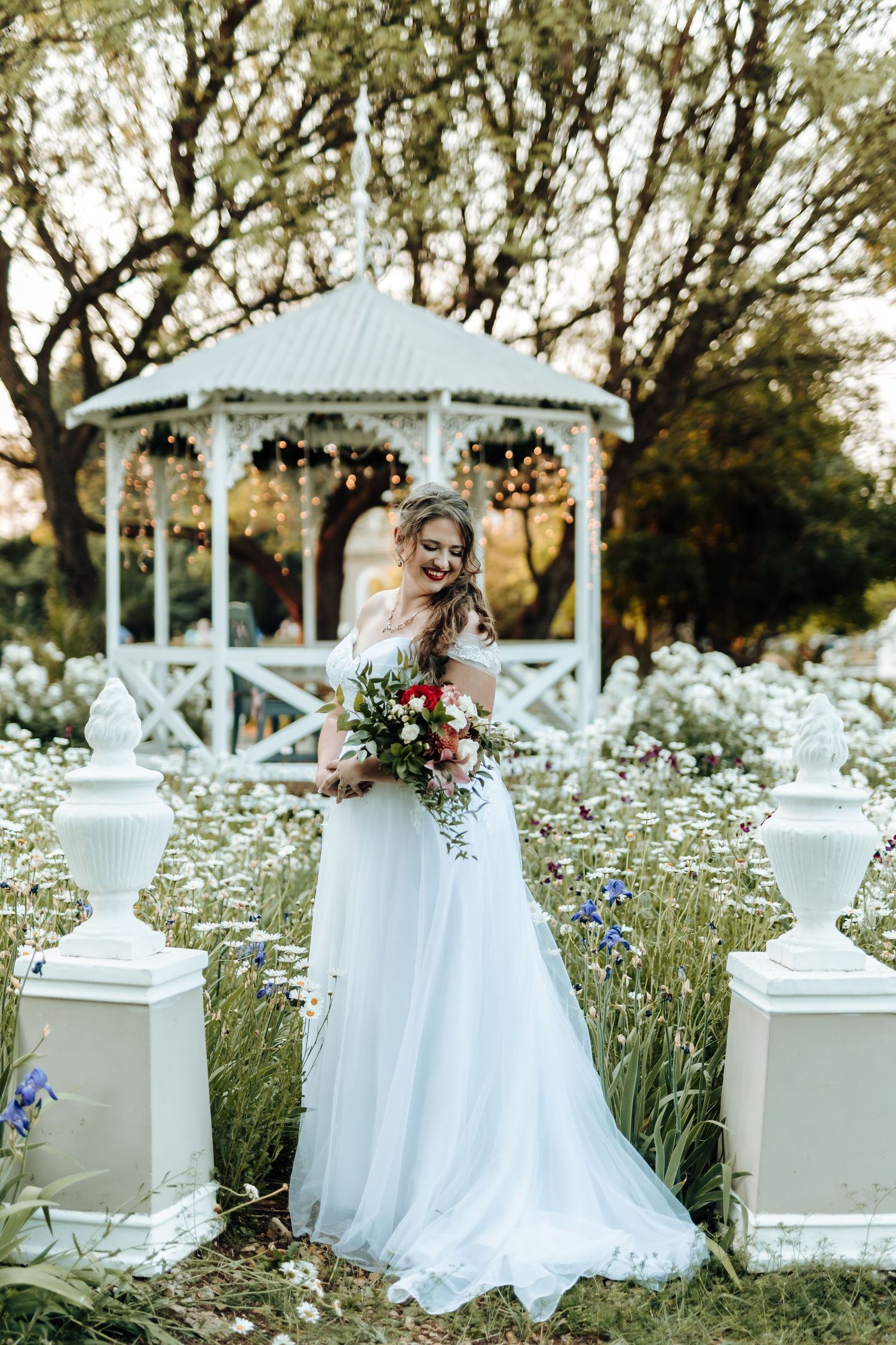 Ethereal bridal portrait by white gazebo surrounded by summer wildflowers and ornate posts.