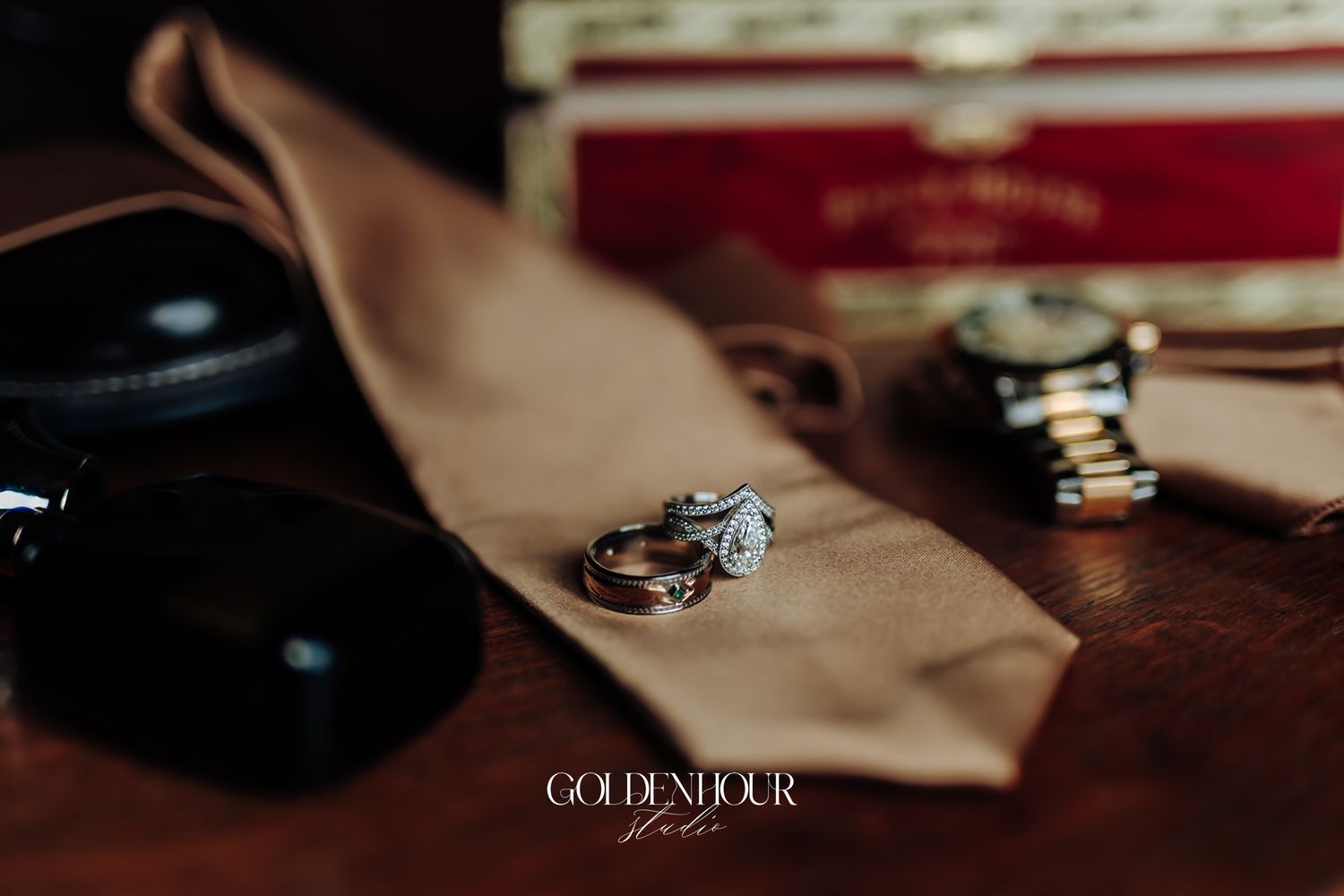 Wedding rings displayed on a tan tie with sunglasses and watch on wooden surface.