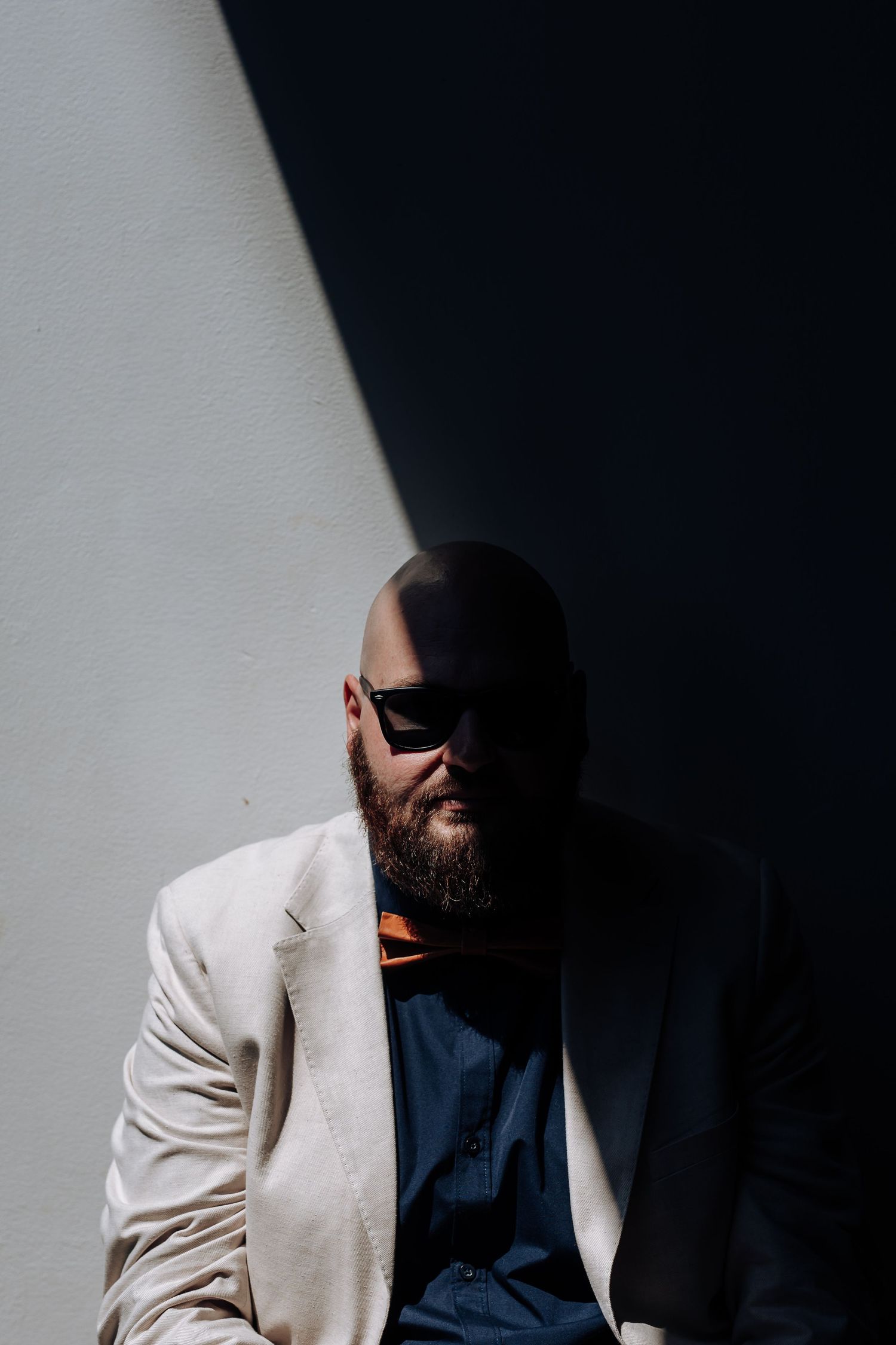 A dramatic portrait in contrasting light shows a person wearing a white blazer and blue shirt against a dark background.