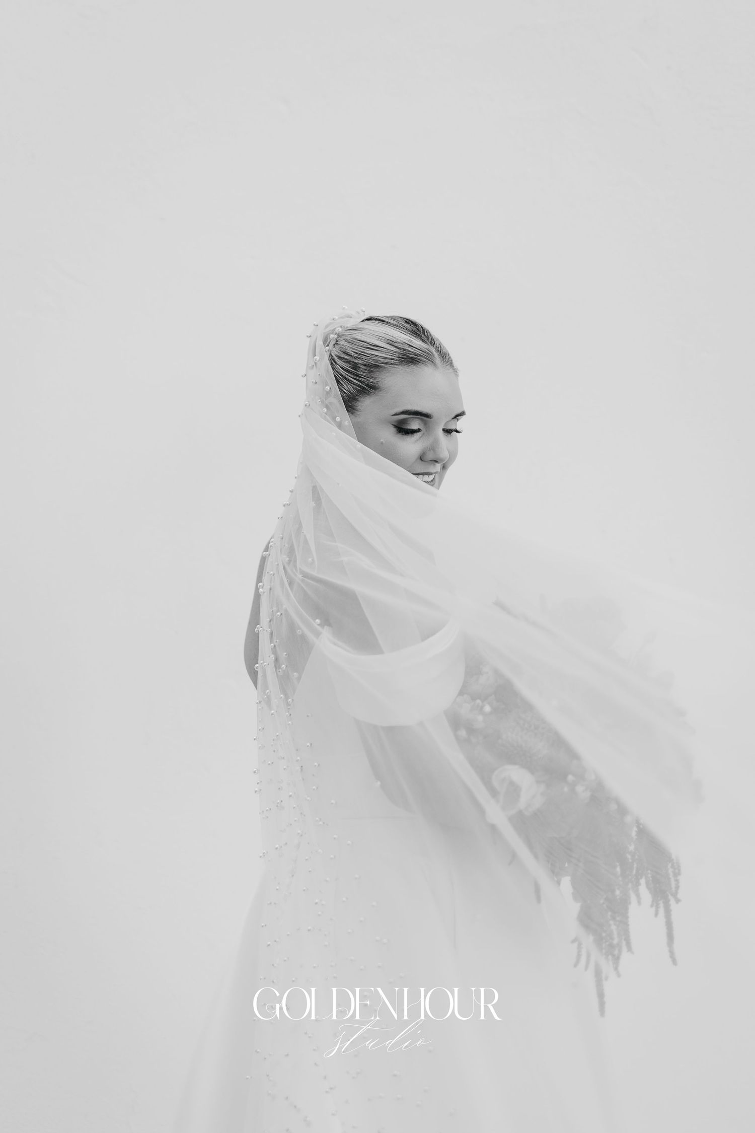 Ethereal black and white bridal portrait with flowing veil creating a dreamy silhouette against light background.