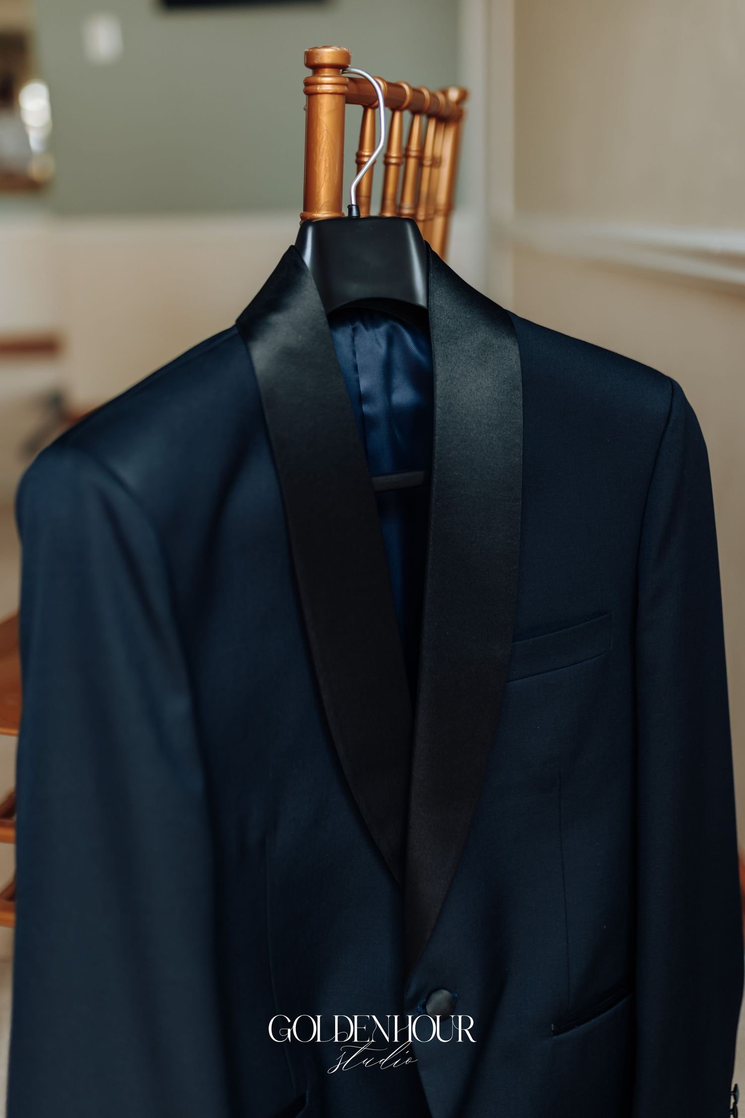 A navy blue tuxedo jacket with black lapels hangs on a wooden hanger against a neutral background.