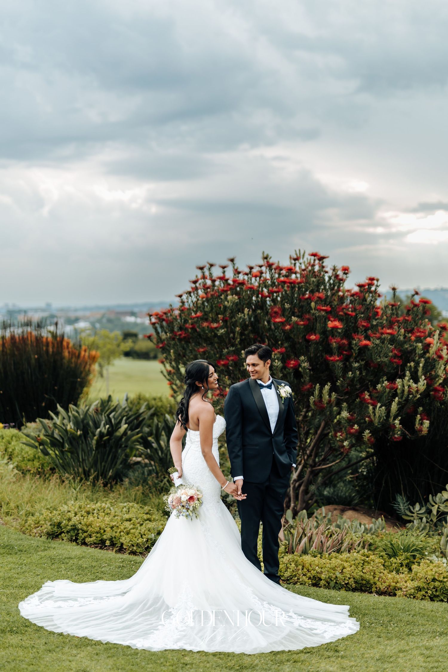 Romantic wedding portraits in a garden setting with blooming red flowers.