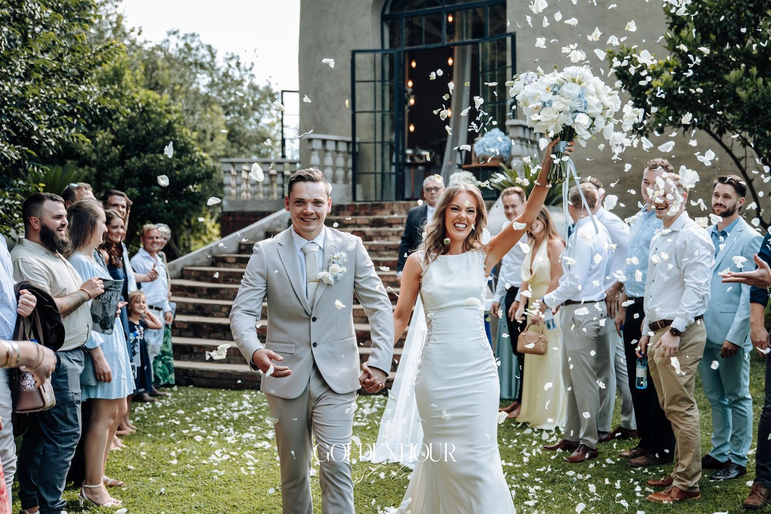 Wedding guests shower the newlyweds with white flower petals as they exit the ceremony in a joyful celebration.