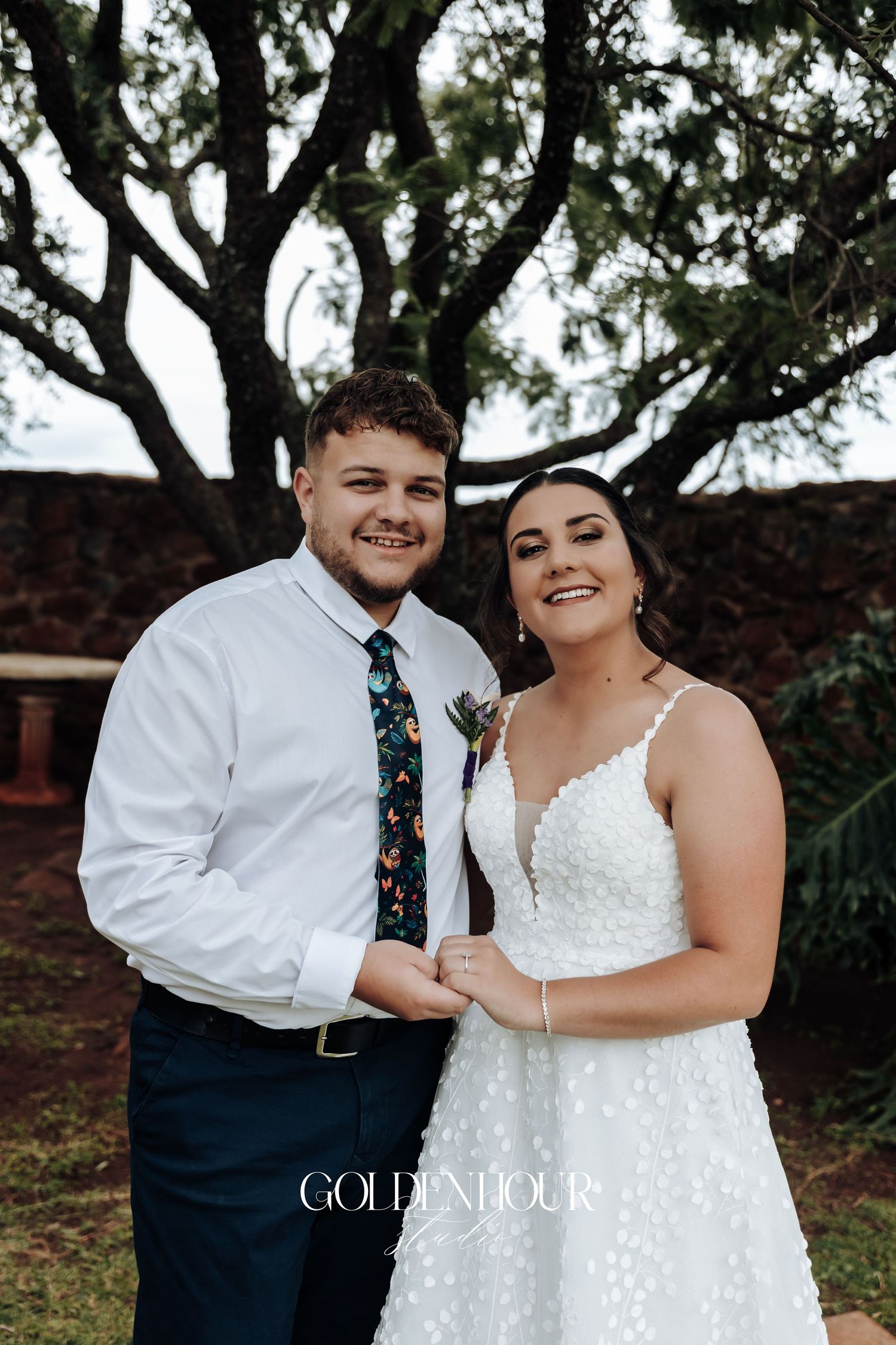 A happy couple poses together outdoors, with the bride wearing a white polka dot wedding dress.