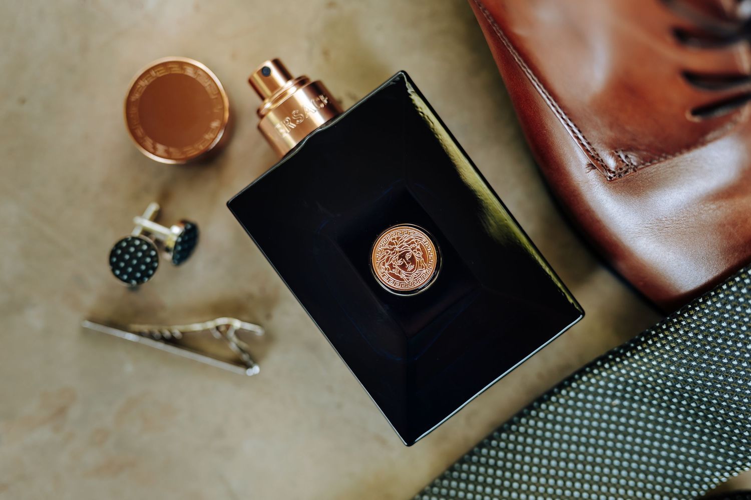 Flat lay of leather accessories including wallet, watch, and tie arranged on textured gray background.