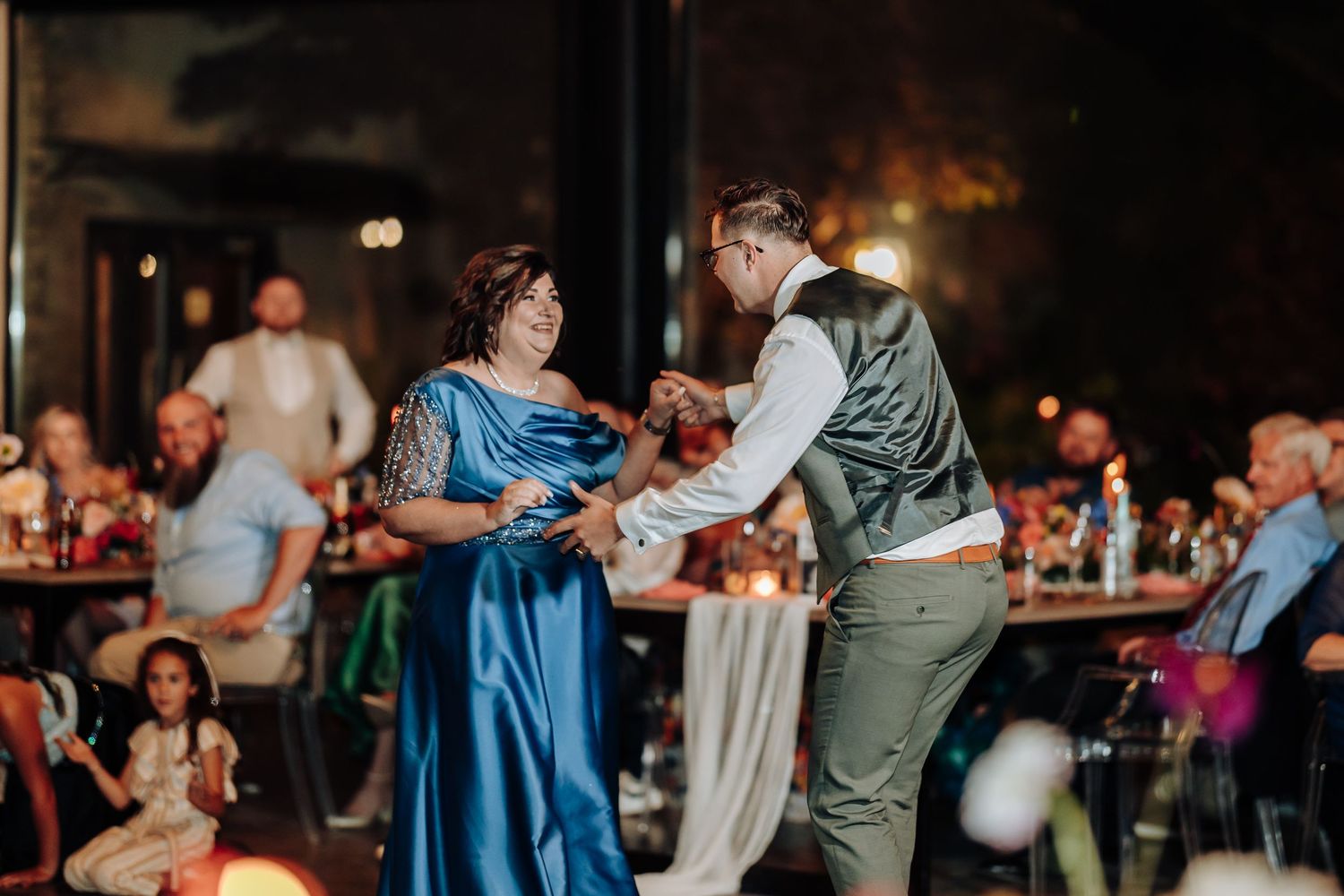 Guests dance together during a wedding reception in a dimly lit venue.