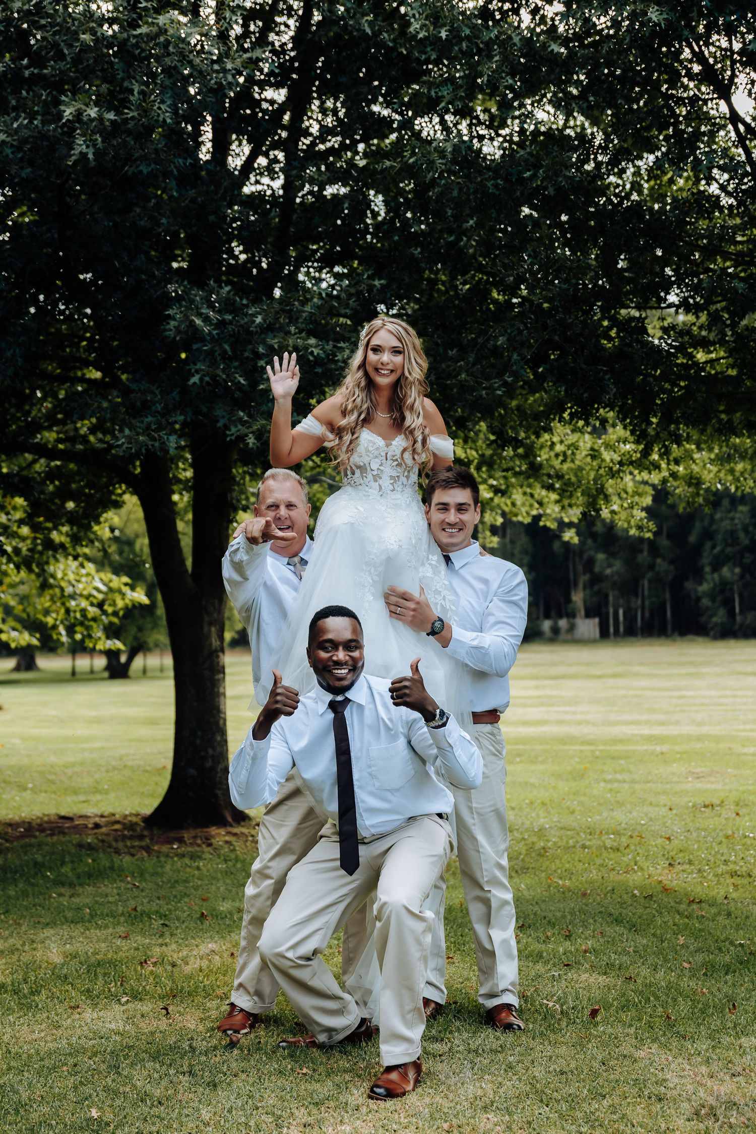 A group in white attire playfully poses for candid photos on a grassy lawn with trees in the background.