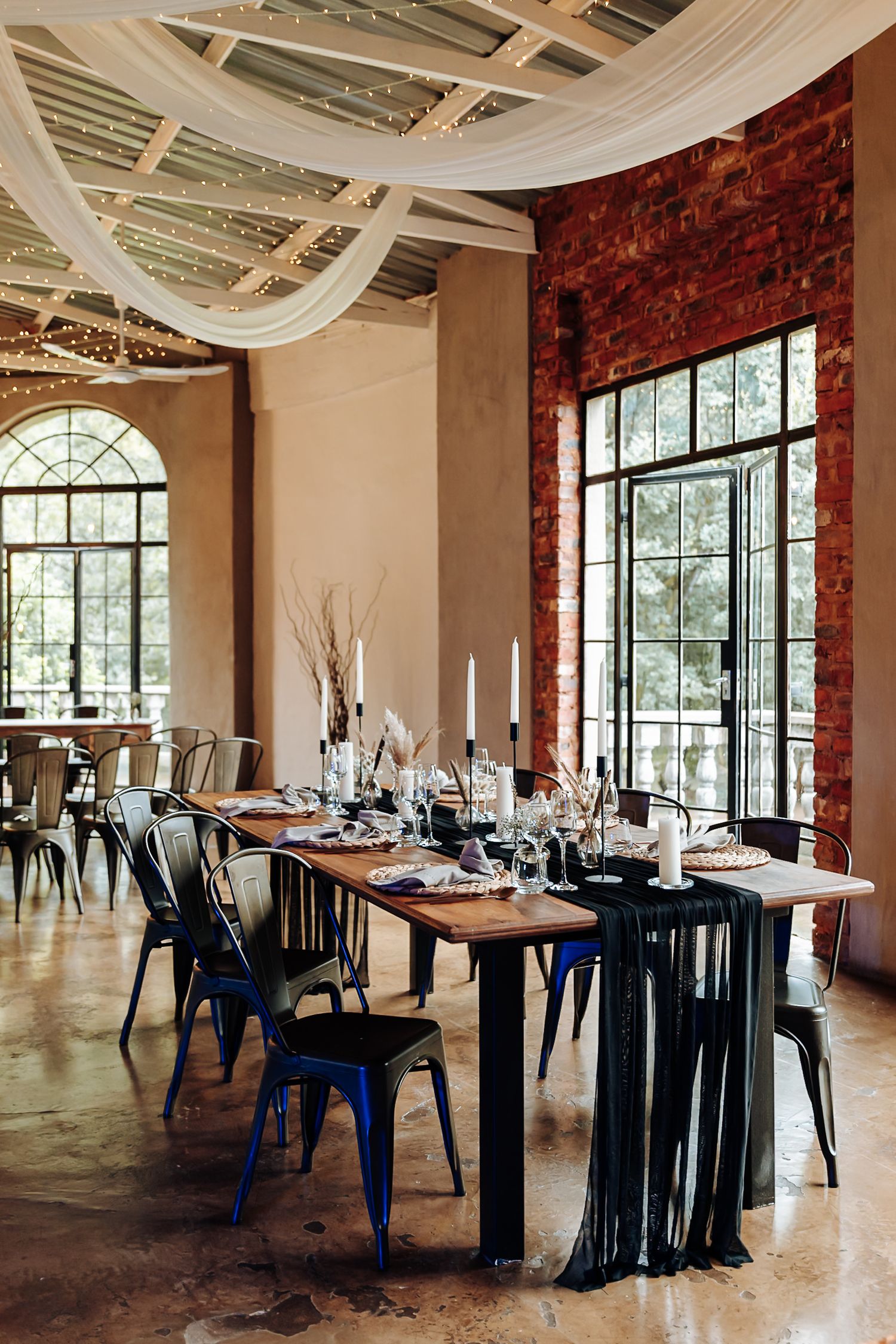 Elegant wedding reception venue with exposed brick walls, white draping, and black chairs set for formal dining.