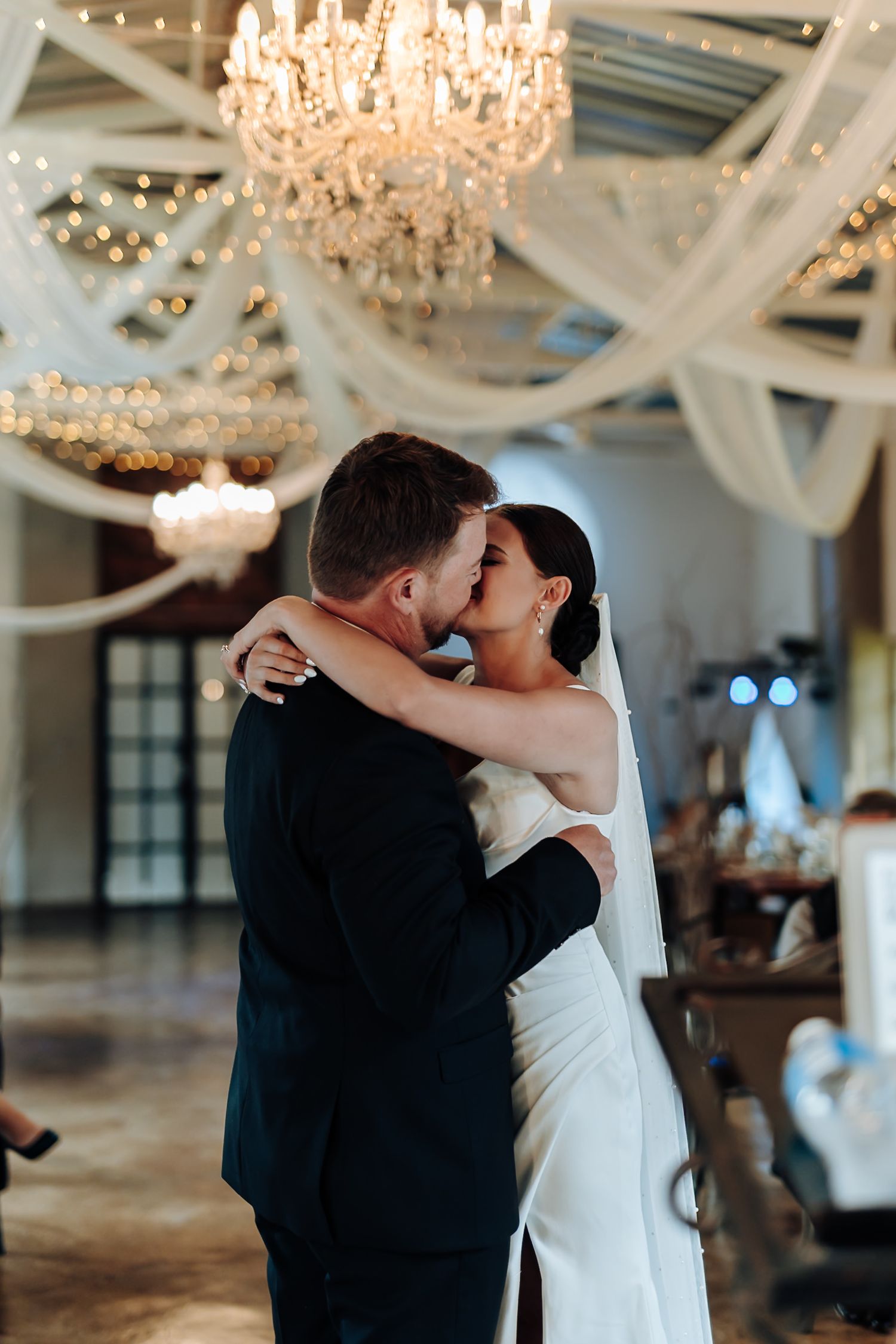 Newlyweds share a romantic first dance under elegant crystal chandeliers in a spacious ballroom venue.