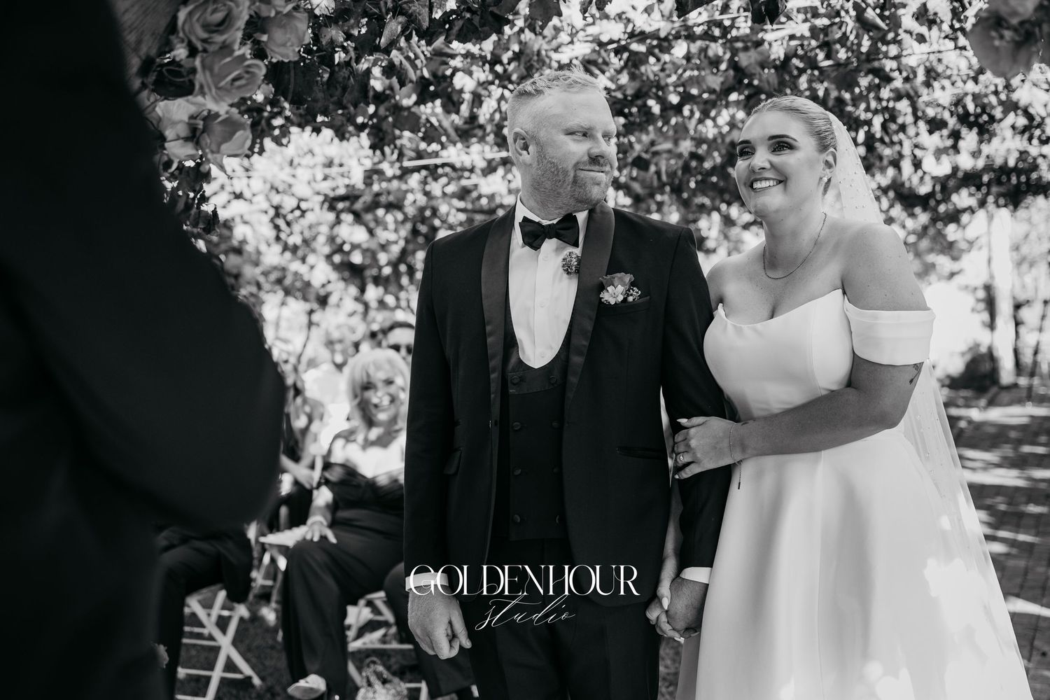 A black and white wedding photograph showing a couple sharing a joyful moment during their outdoor ceremony.