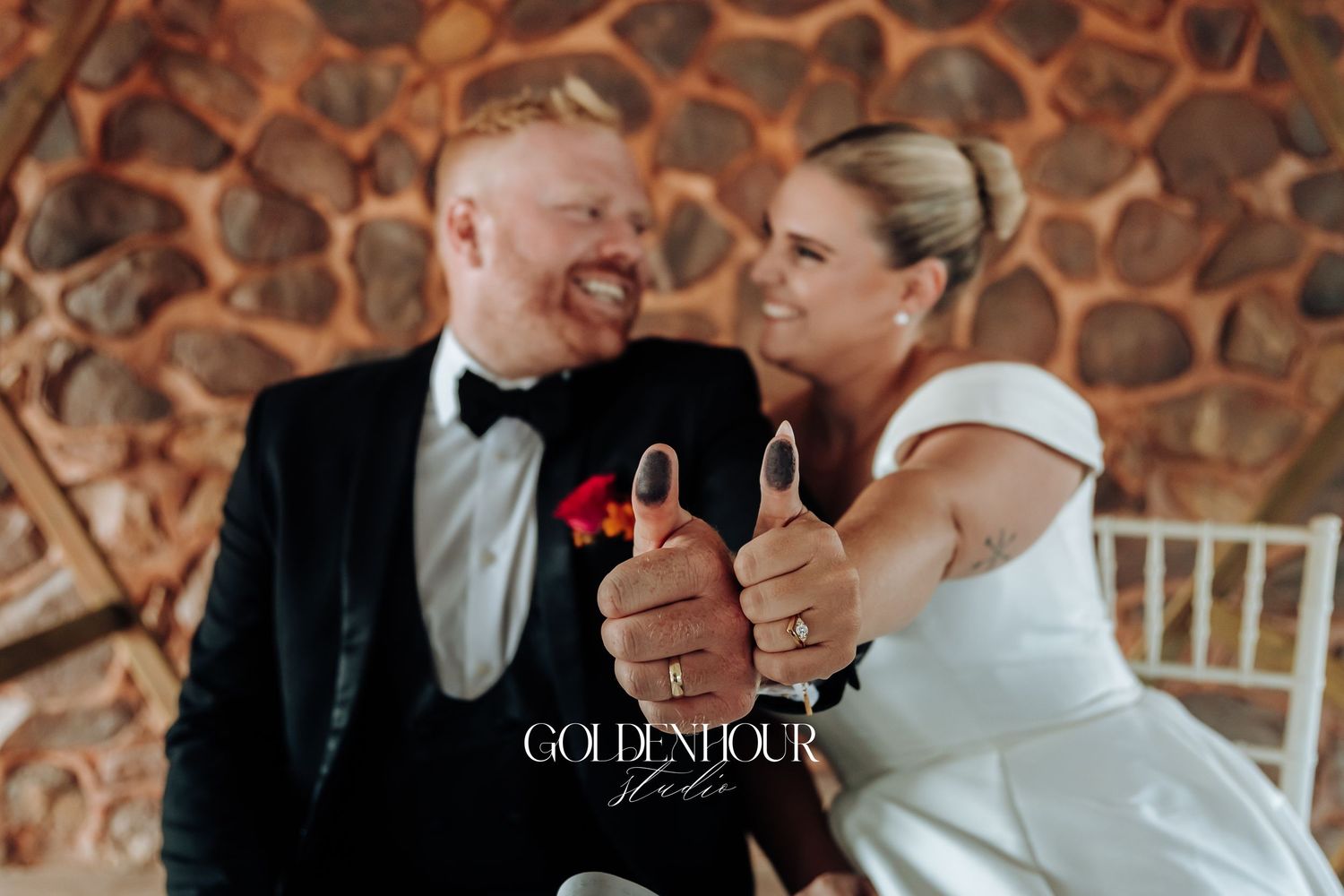 A couple shares an intimate moment during their wedding ceremony against a rustic stone wall backdrop.