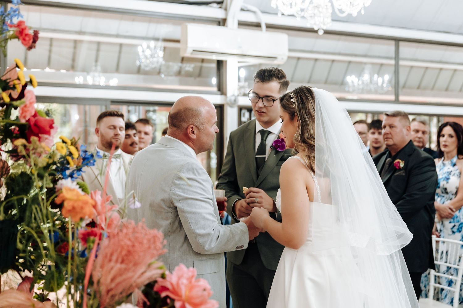 Elegant wedding celebration with floral decorations and crystal chandelier in a bright indoor venue.