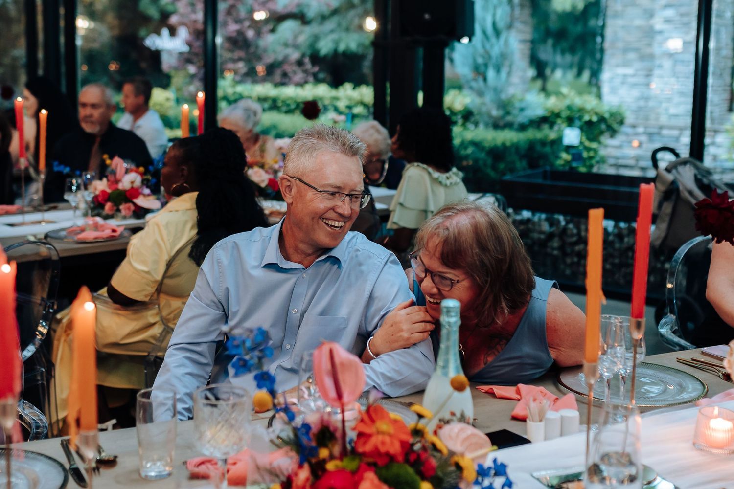 Outdoor wedding reception dinner with red candles and floral centerpieces at dusk.