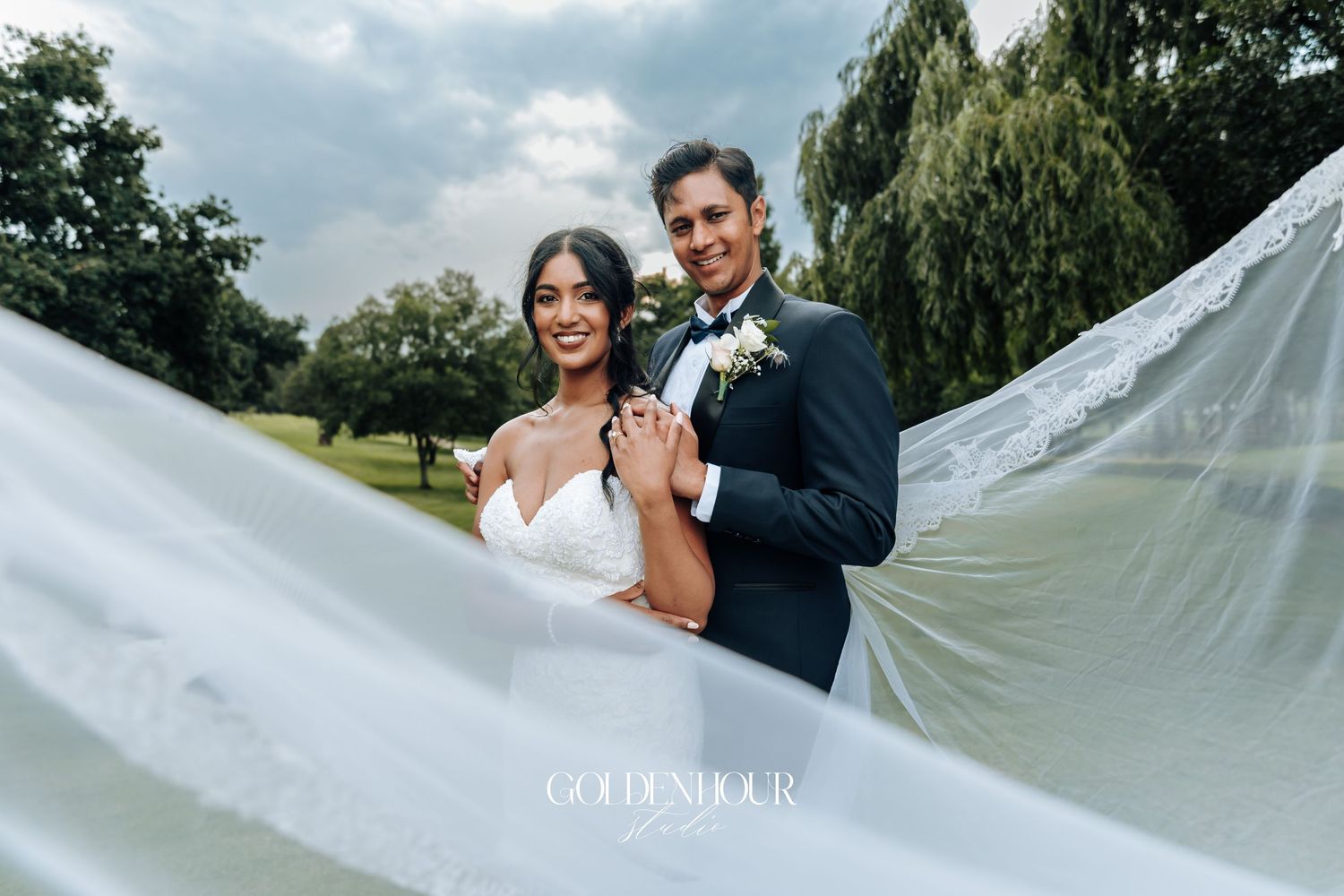 Wedding couple with flowing veil against dramatic cloudy sky.