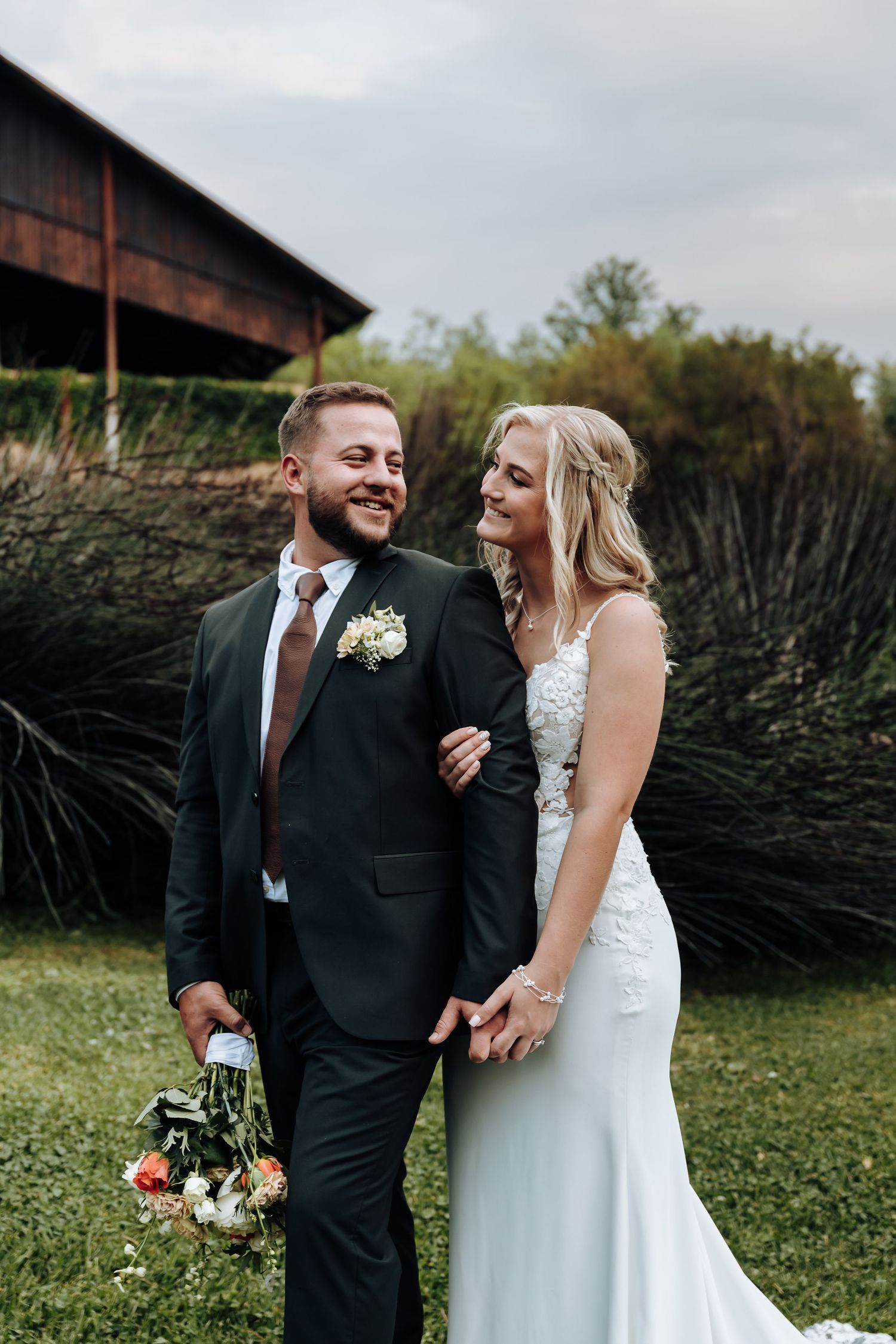 A couple shares joyful moments together during their outdoor wedding celebration against a rustic barn backdrop.