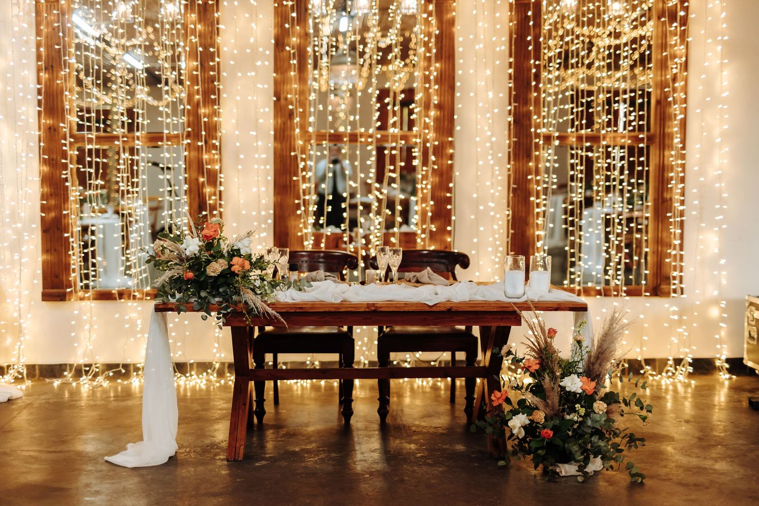 String lights create a romantic glow in an elegant wedding reception venue with floral arrangements and white decor.