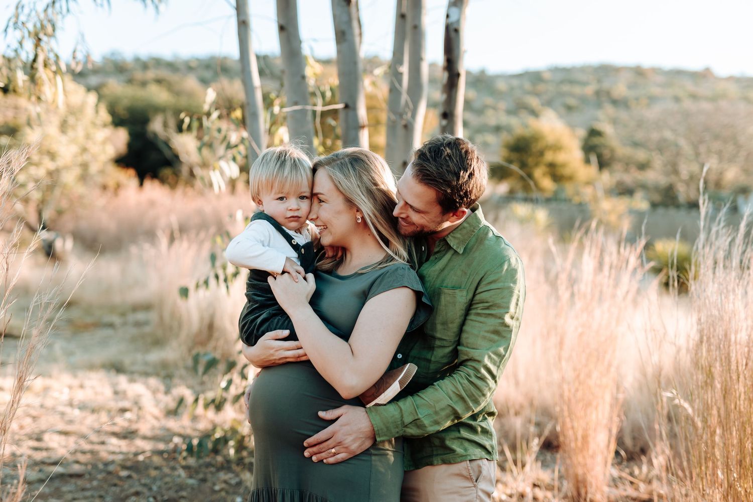 Two people embrace with affection in a sun-drenched field at sunset against a desert landscape backdrop.