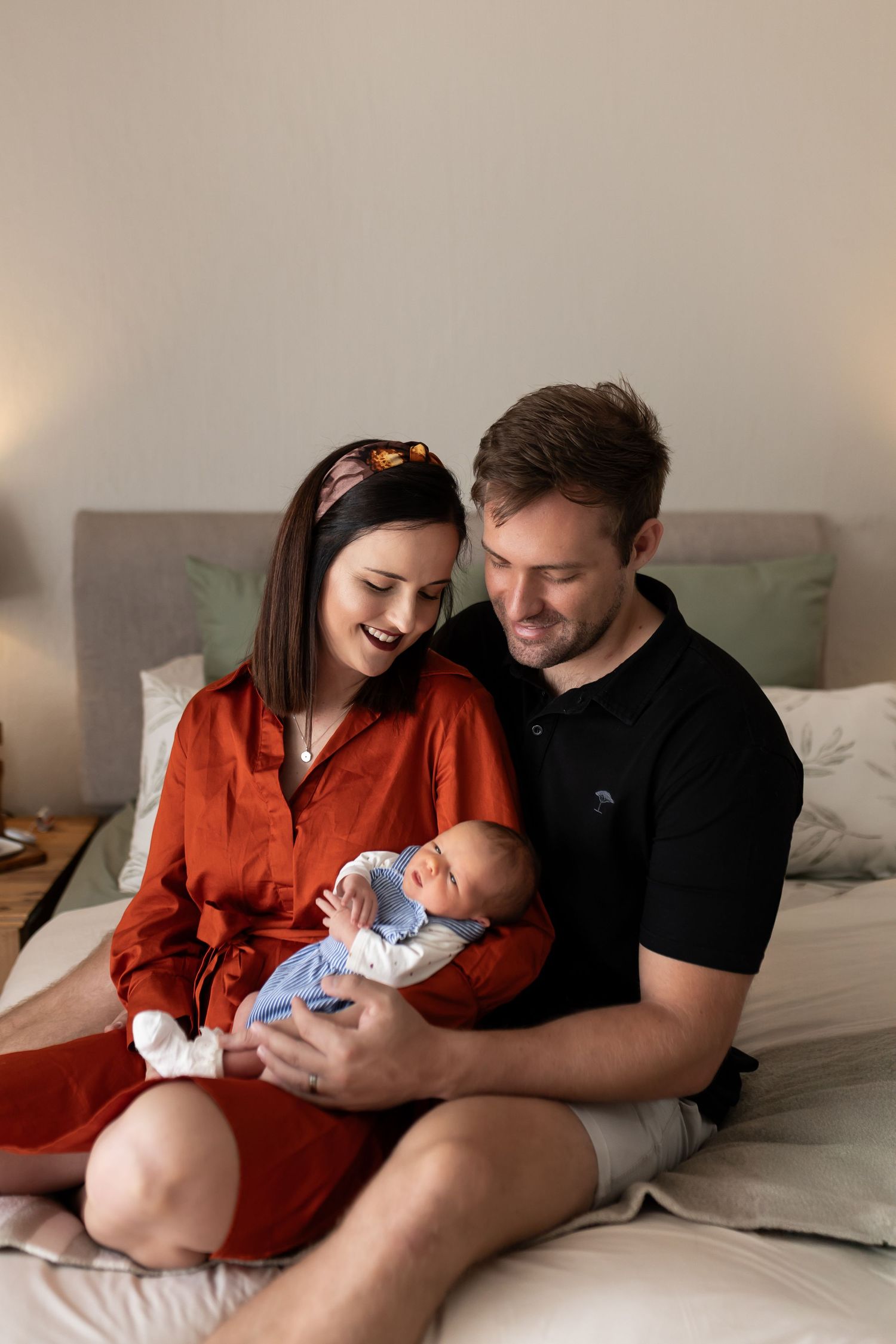 A couple sits on a bed holding a newborn baby while sharing a tender moment together in multiple related photos.