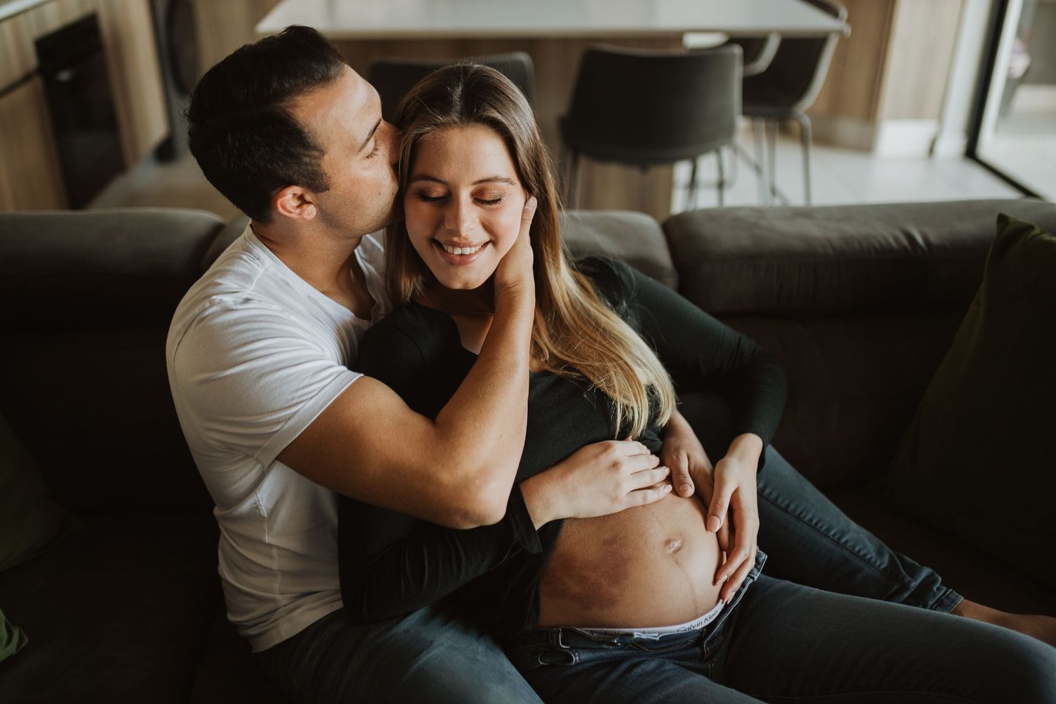 Couple snuggling and laughing together on a dark couch during an intimate lifestyle photoshoot.