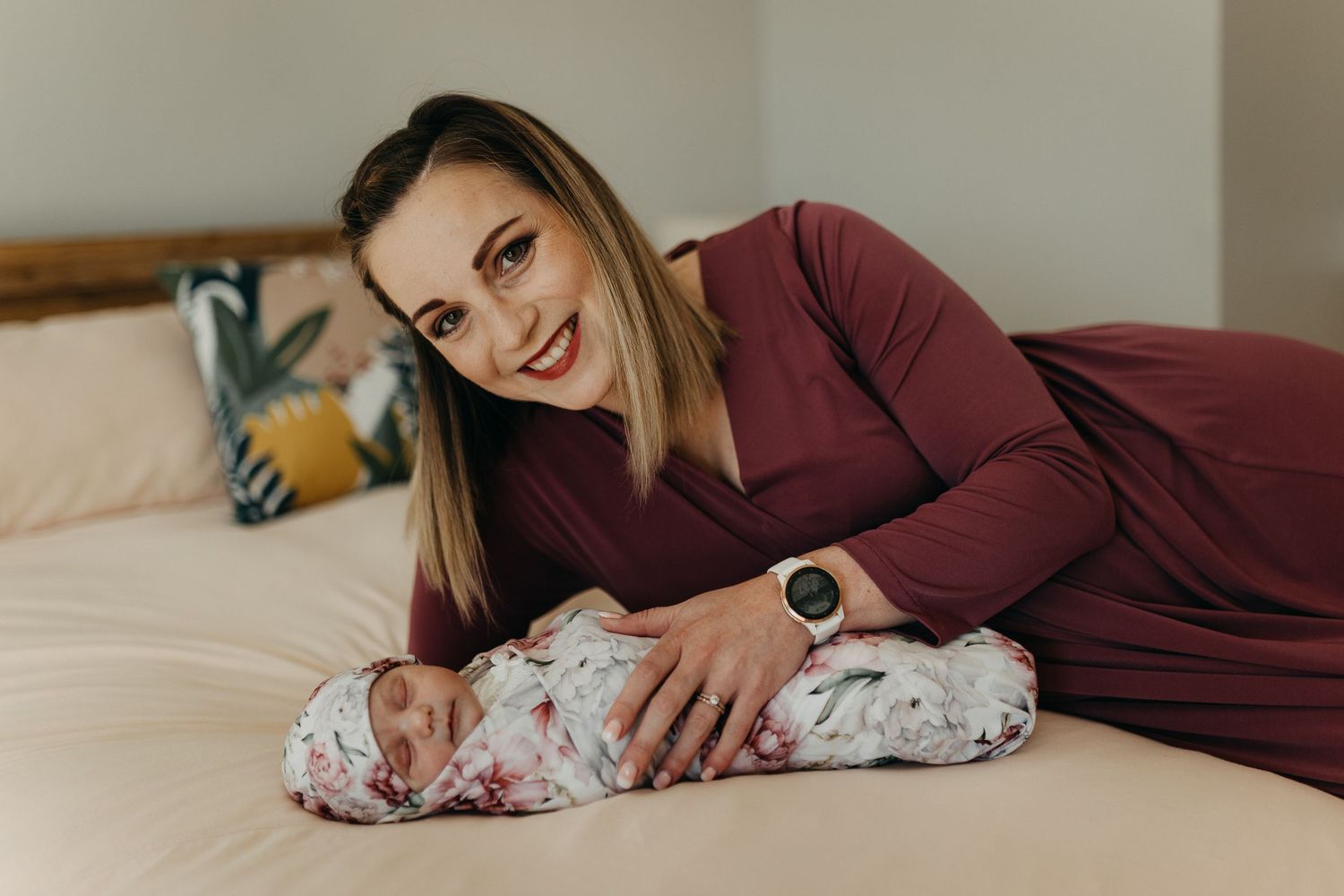 A person in a maroon dress relaxes on a beige bed with floral print baby blanket.