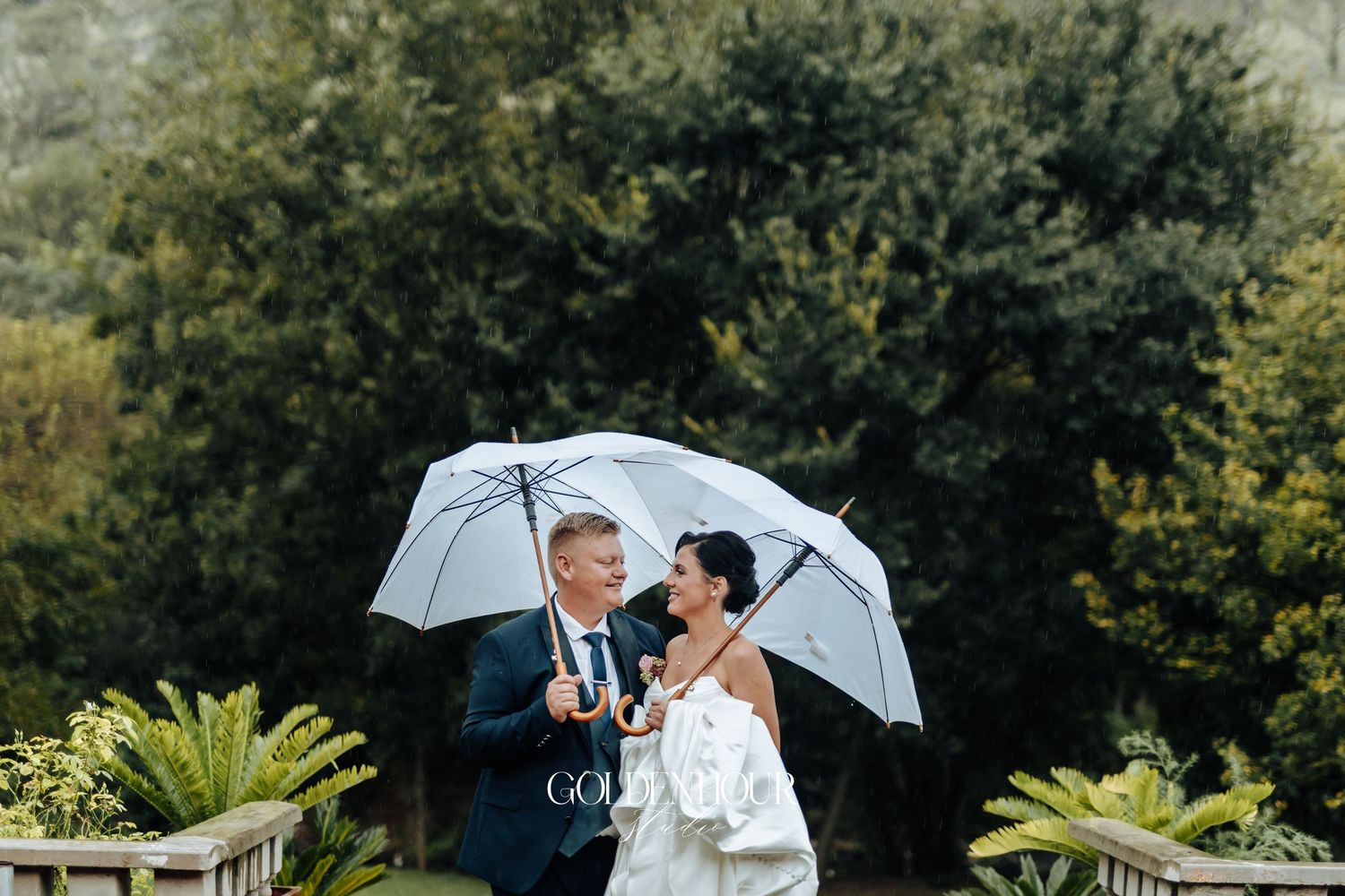 Bride and groom sharing romantic moment under white umbrellas in lush garden wedding setting.