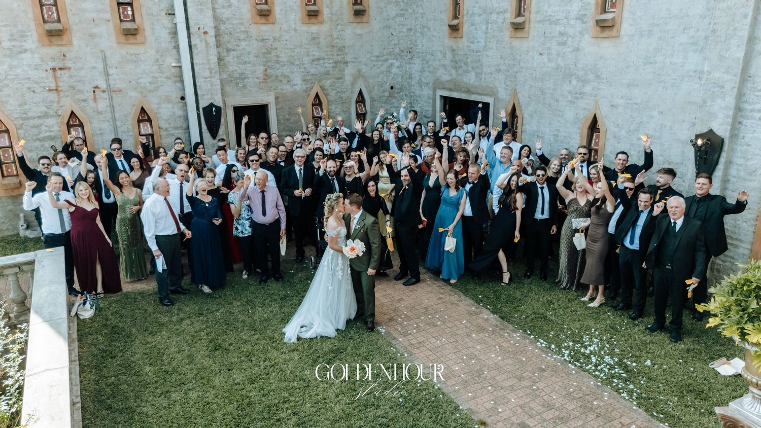 Large wedding group photo with bride and groom surrounded by all guests outside a castle venue.