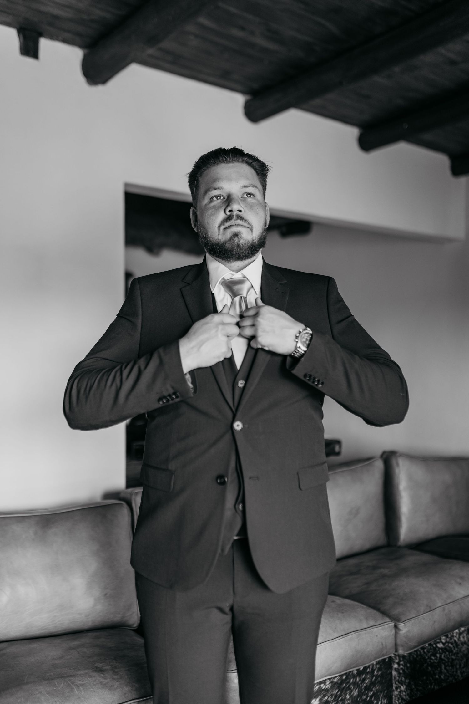 Black and white portrait of person adjusting tie while wearing formal suit with determined expression.