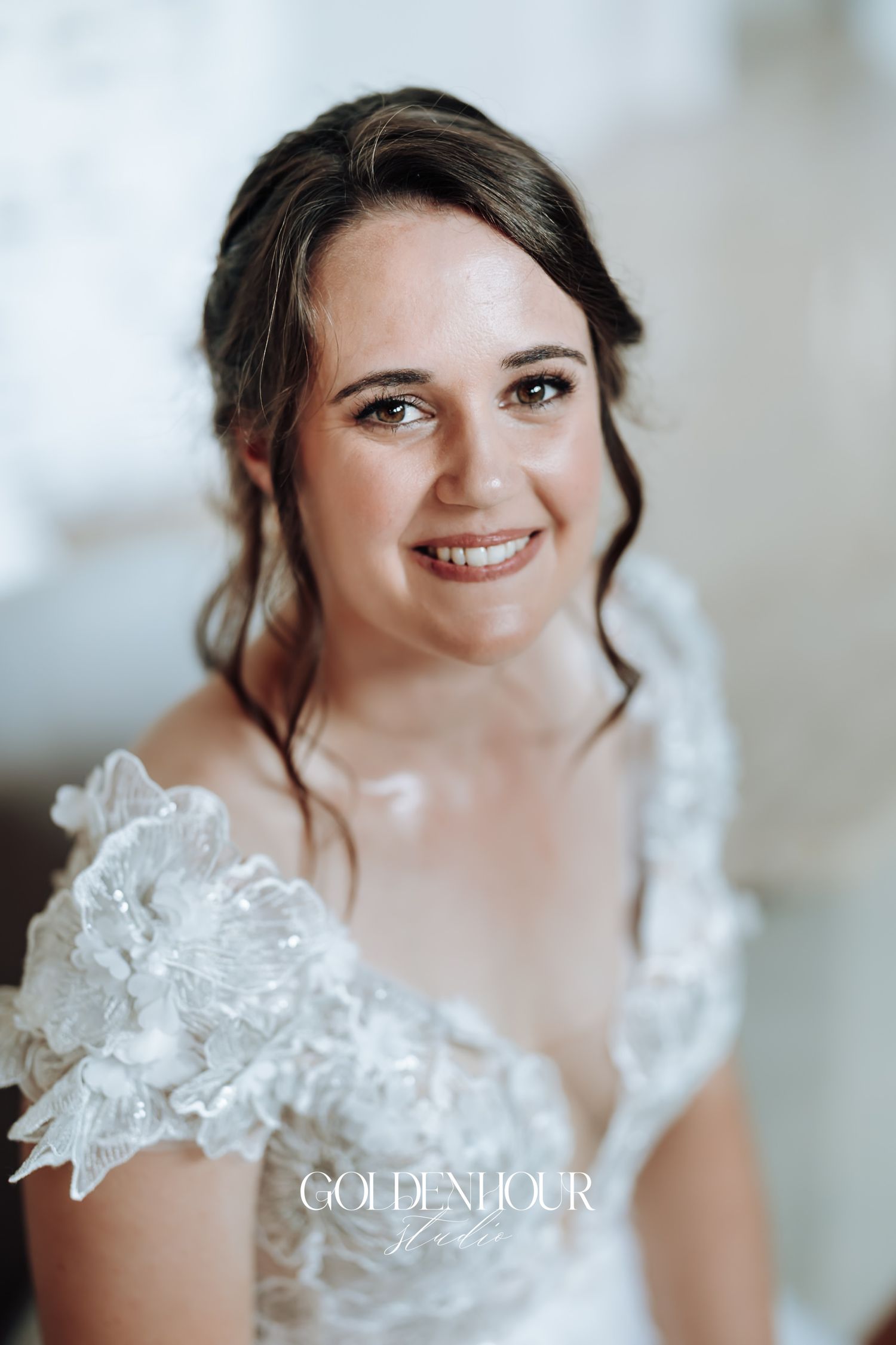 Smiling bride in a floral lace wedding dress with an elegant updo hairstyle.
